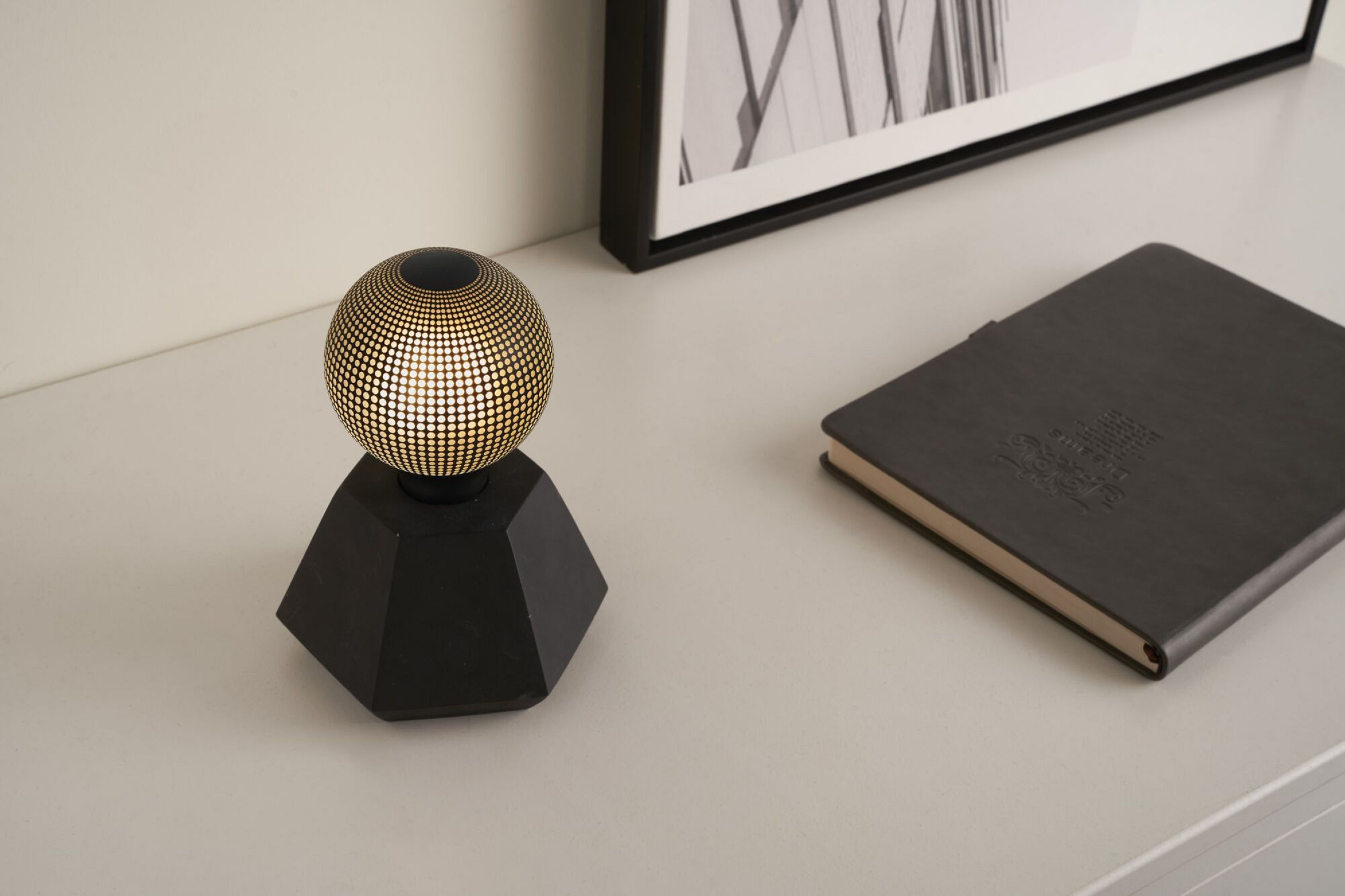 Dekoracyjna lampa z czarną podstawą i złotą kulą w kropki. W pobliżu notatnik.