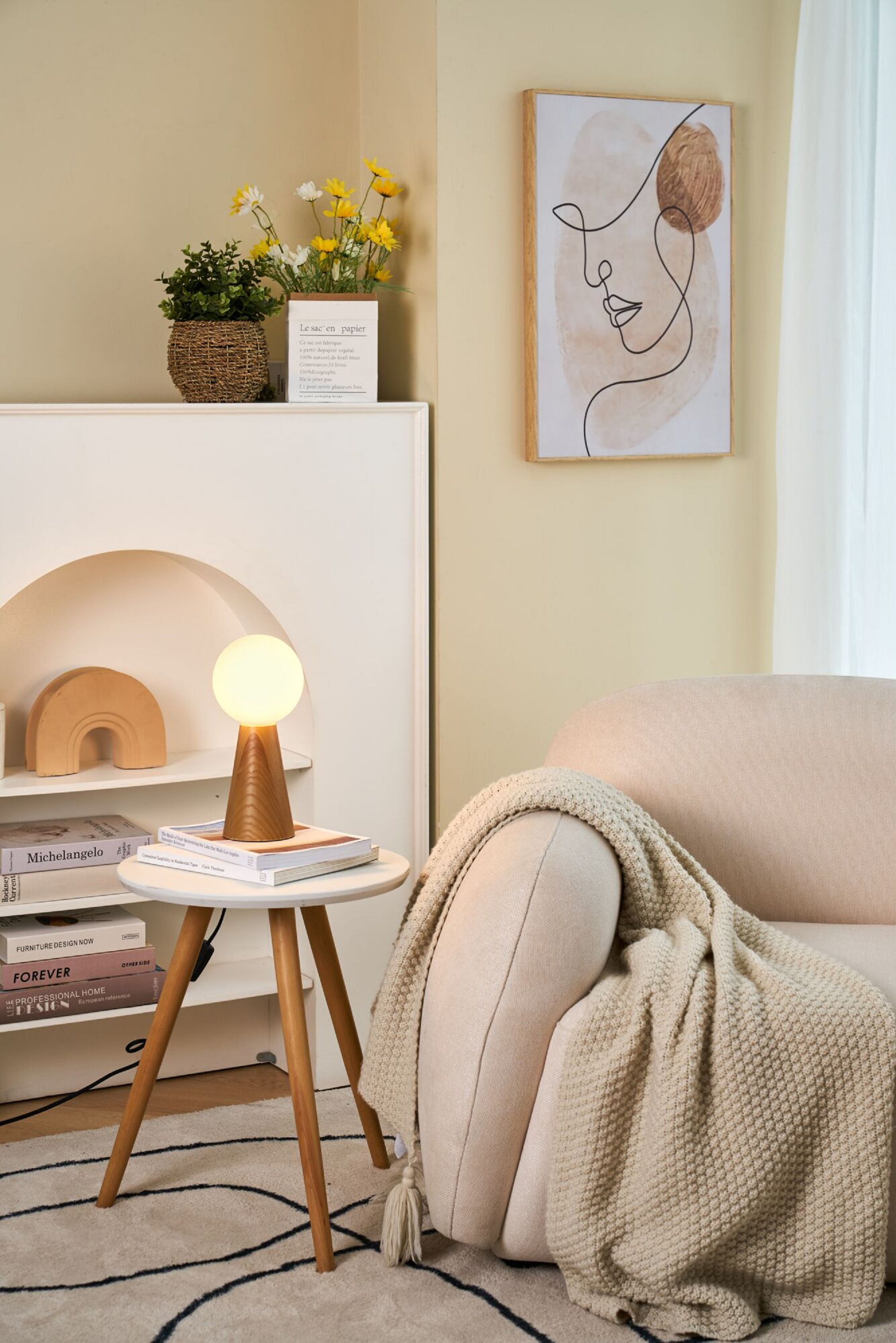 Lampa na stoliku, sofa z kocem, dekoracje na półce i oprawione dzieło sztuki.