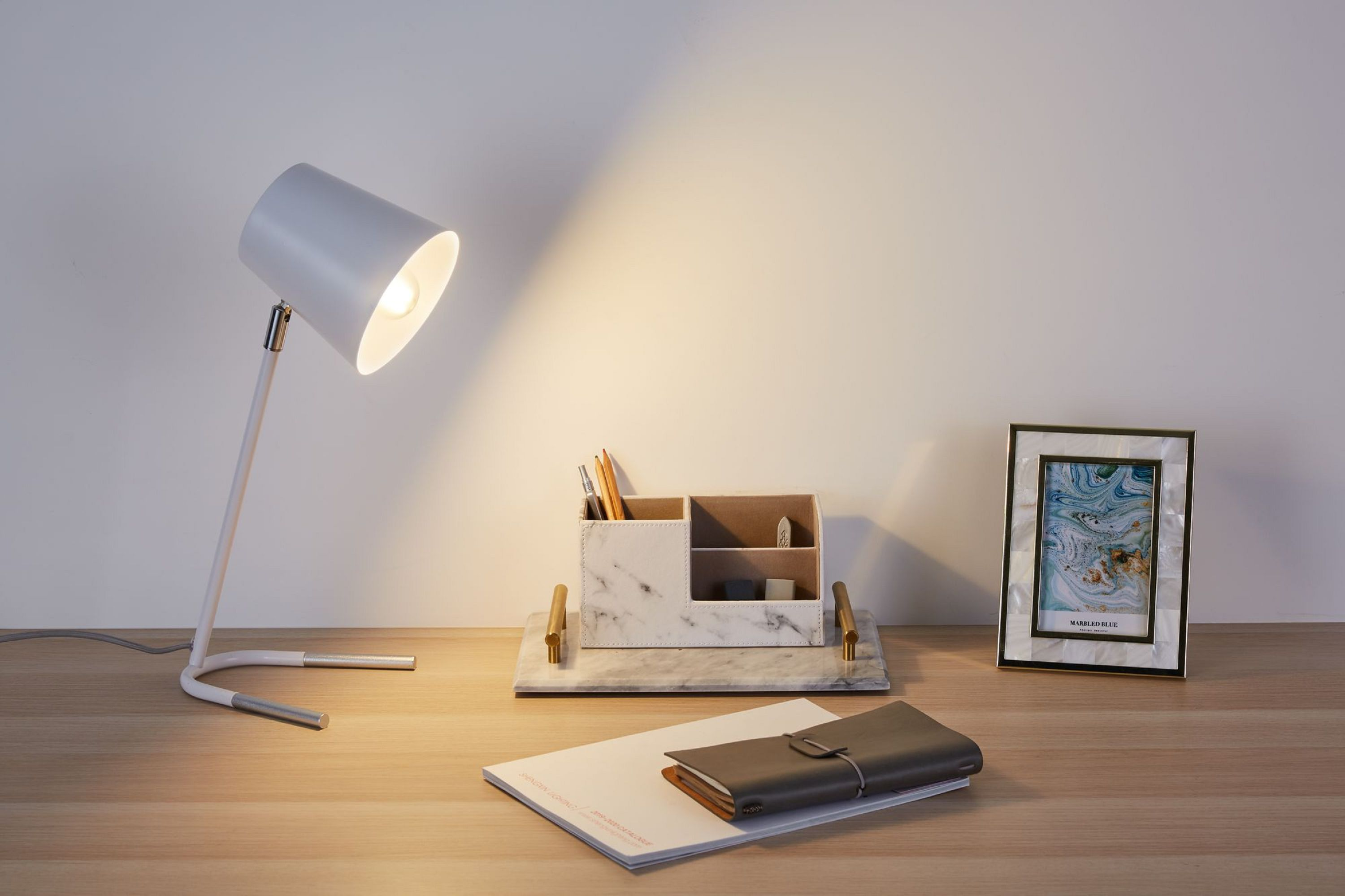 Ein Schreibtisch mit Lampe, Organizer, Notizblock und Bilderrahmen; warmes Licht.