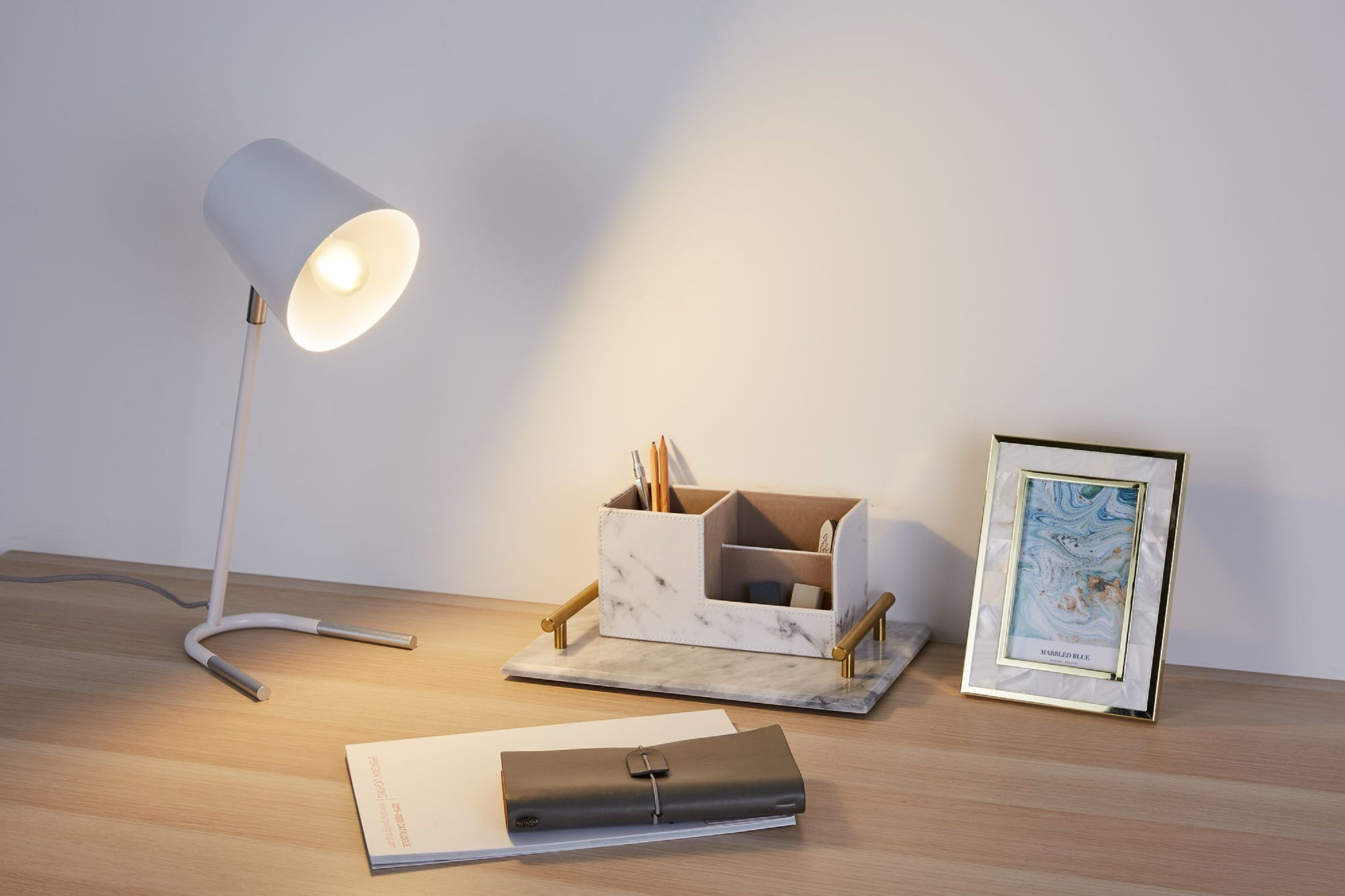 Schreibtisch mit Lampe, Stifthalter, Notizblock und Bilderrahmen.
