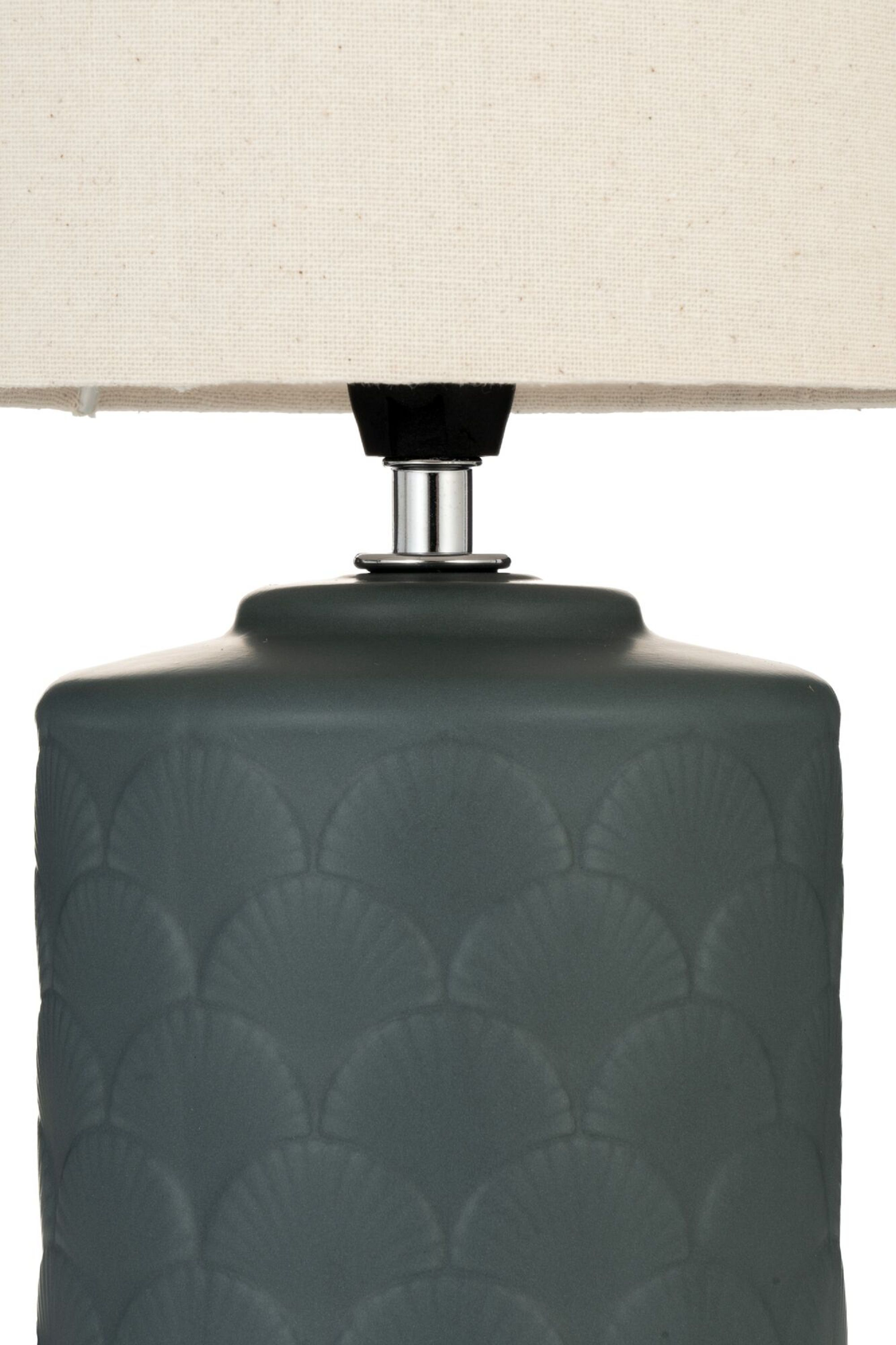 Zbliżenie ciemnoszarej ceramicznej lampy z beżowym abażurem. Wzór muszli na podstawie.