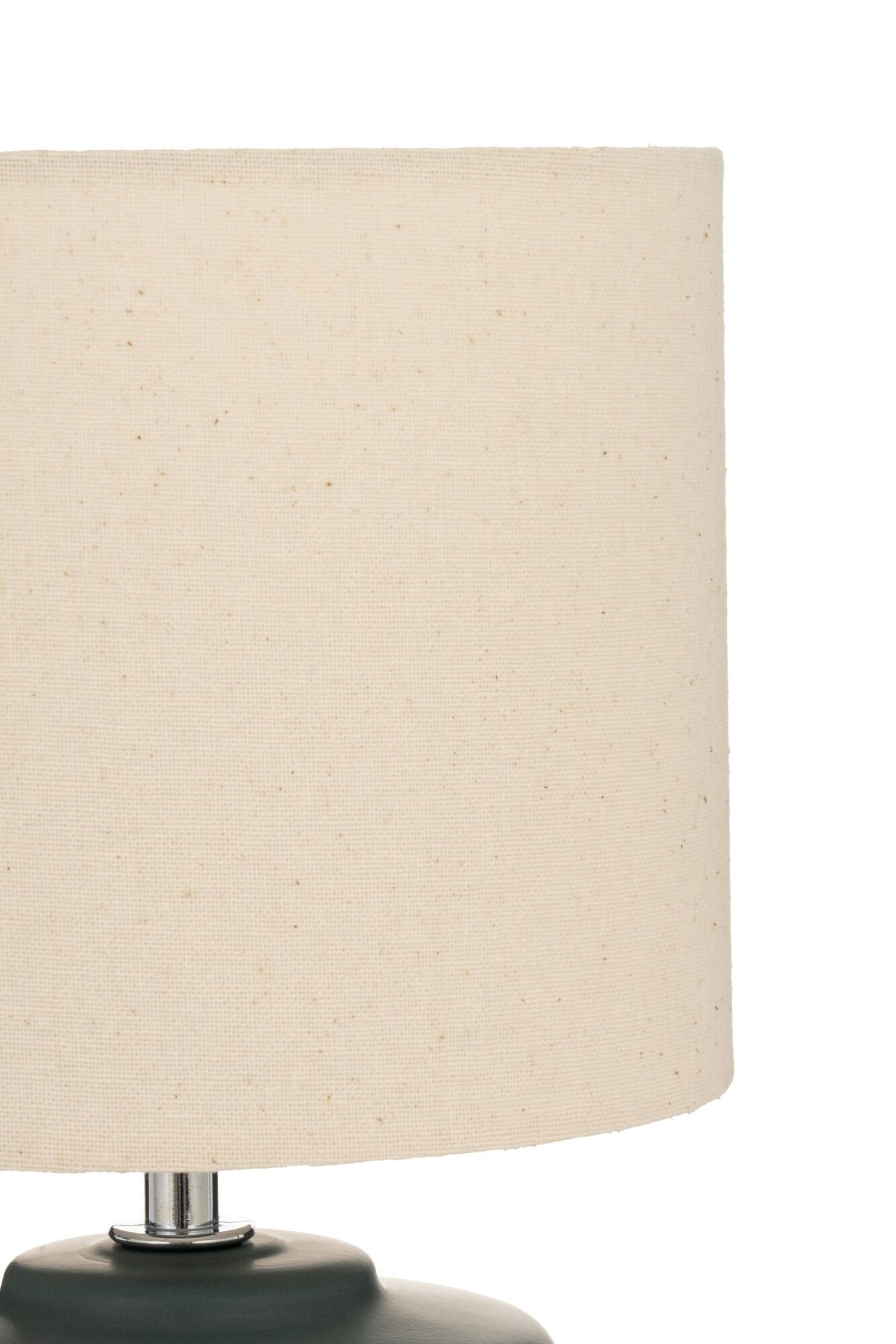 Zbliżenie kremowego abażuru na zielonej podstawie. Białe tło.