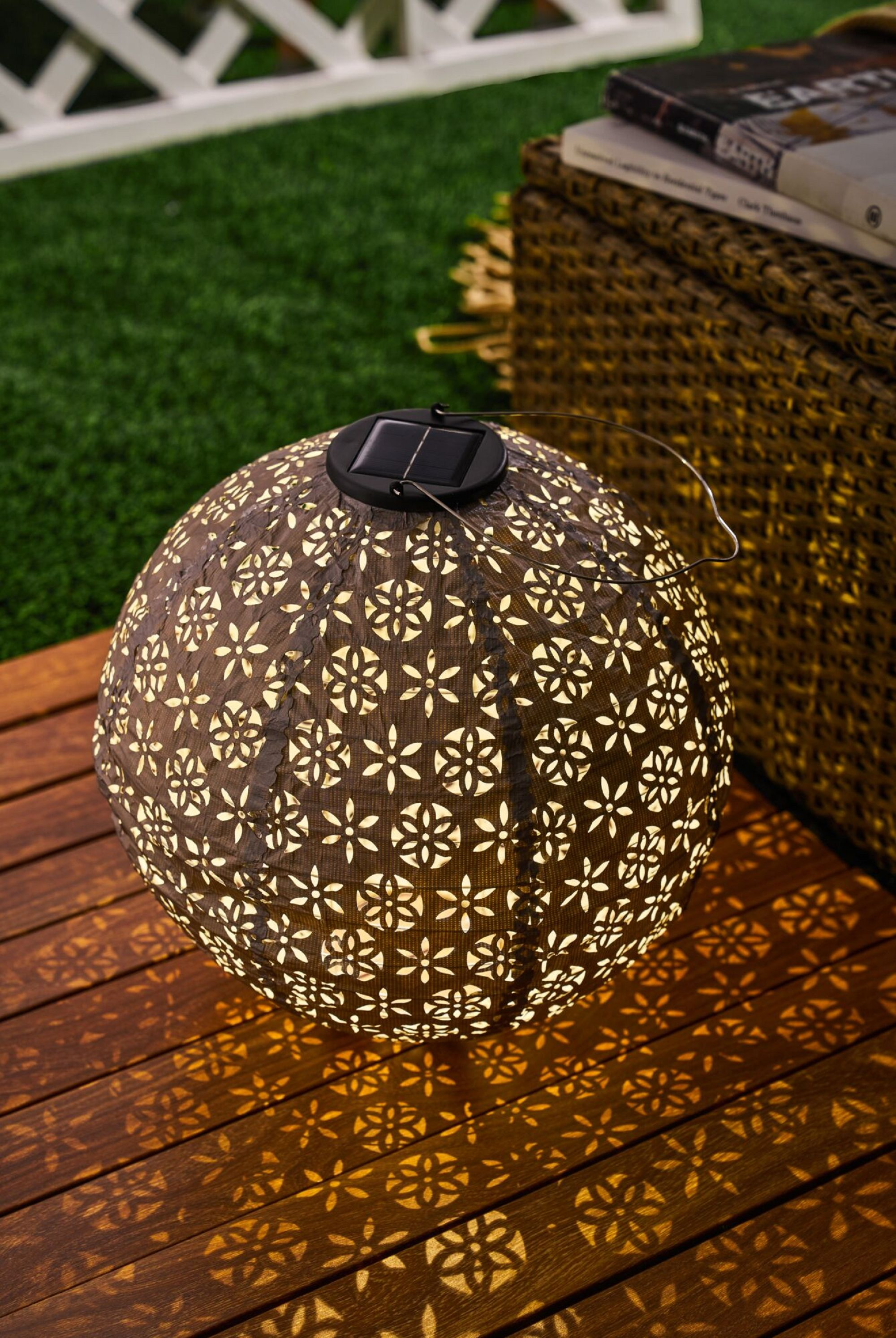 Latarnia solarna na drewnianej powierzchni. Latarnia jest okrągła z kwiatowymi wzorami.