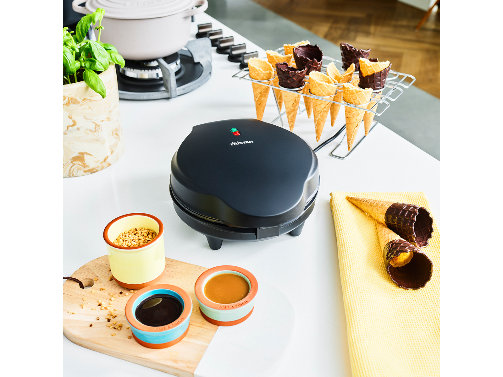 Küchenszene. Waffeleisen, Waffelhörnchen, Schüsseln mit Soßen und Toppings und ein Kochtopf.