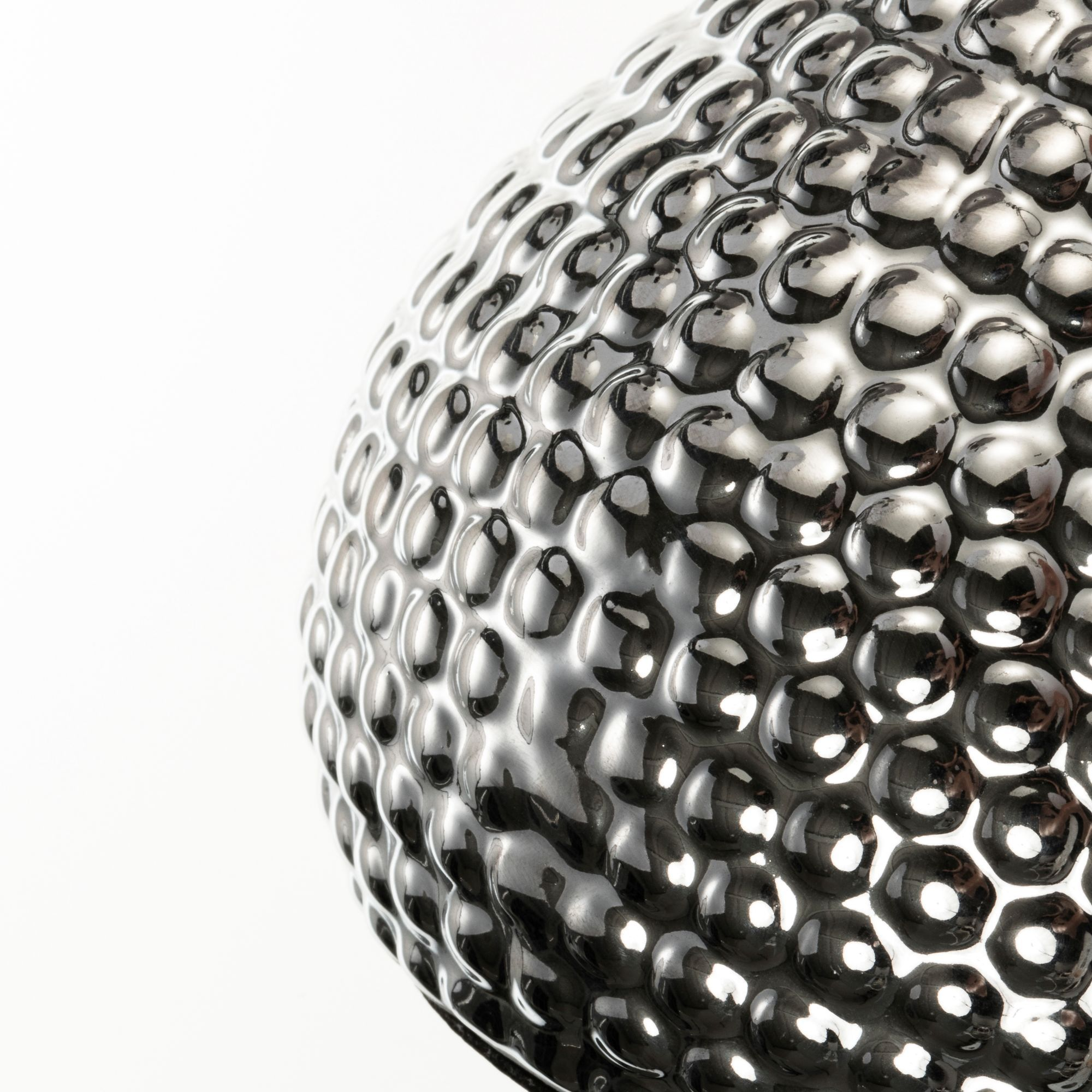 Zbliżenie błyszczącego, srebrnego obiektu w kształcie kuli o chropowatej fakturze, białe tło.