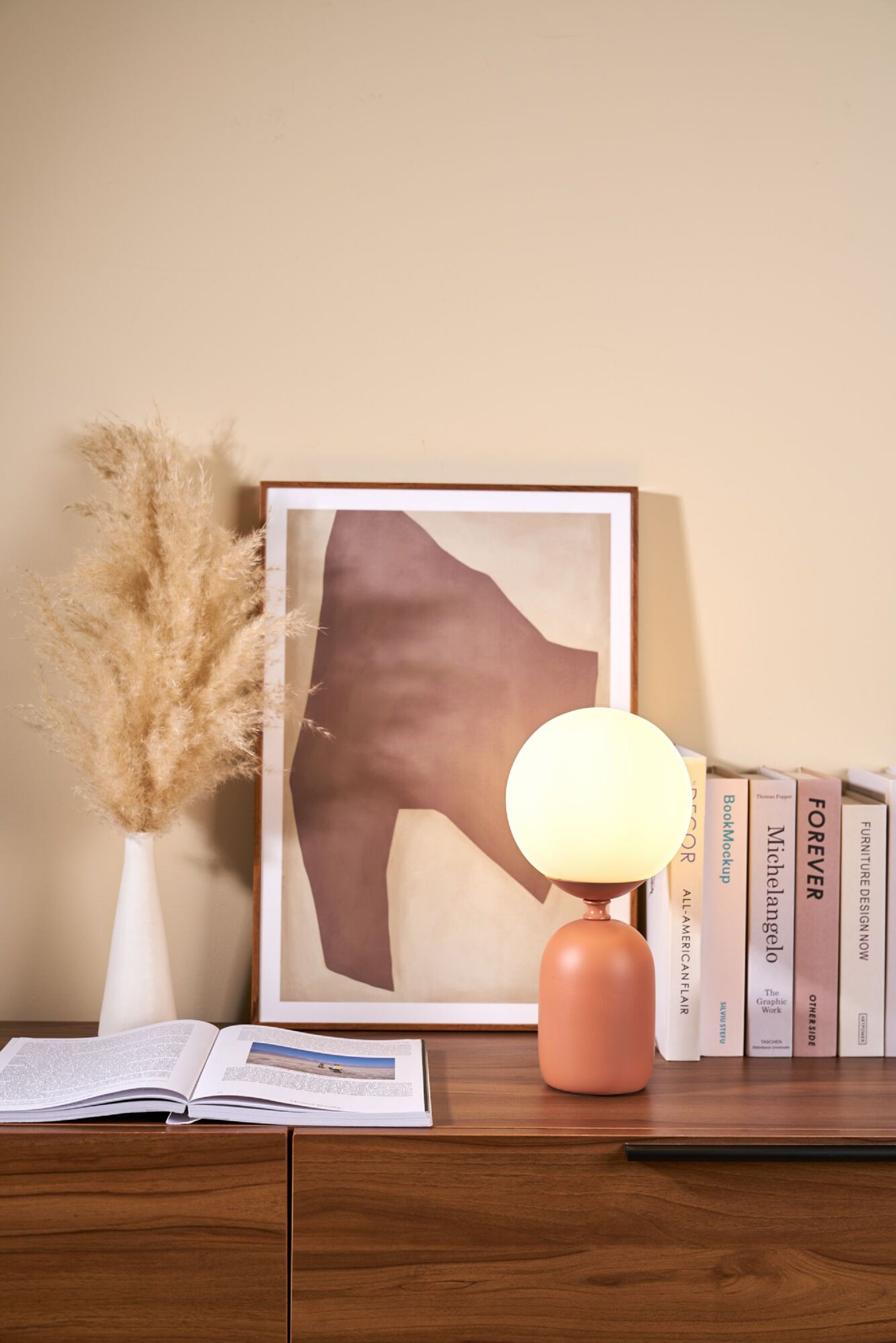 Lampa na drewnianej powierzchni z książkami i wazonem. Beżowa ściana w tle.