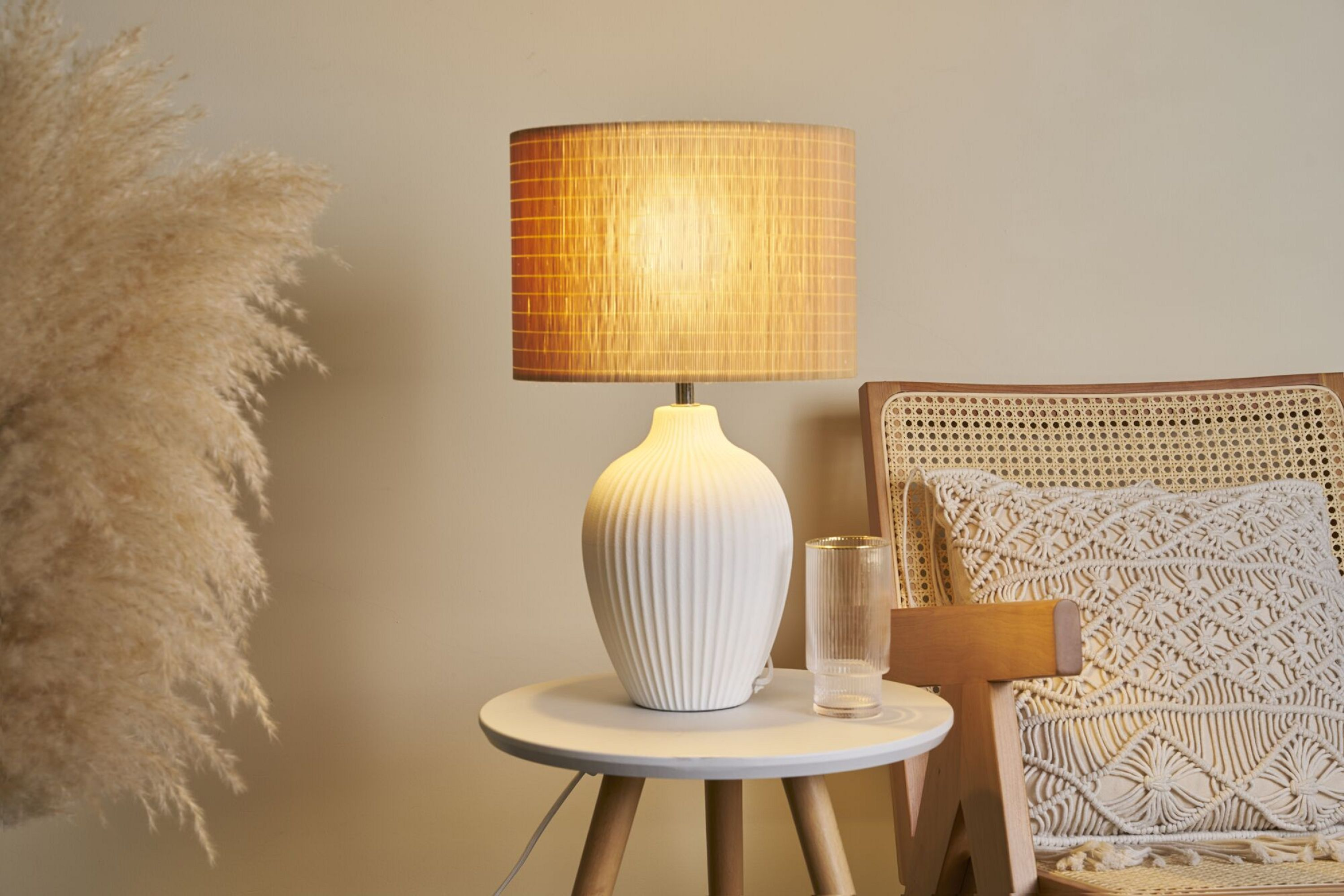 Biała lampa z bambusowym abażurem na białym stoliku. Widoczny jest również wazon i krzesło.