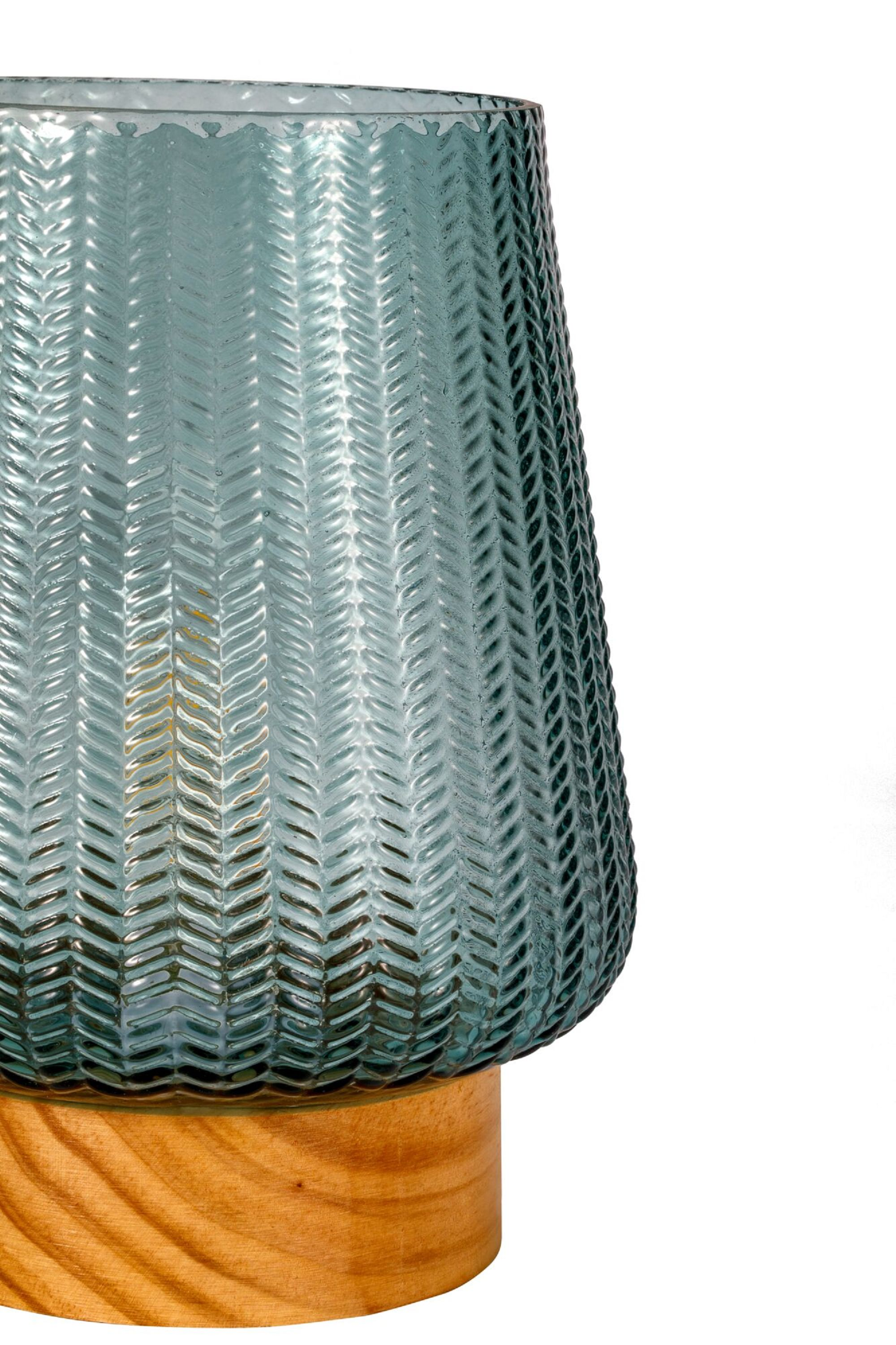 Zielono-niebieska szklana lampa z drewnianą podstawą na białym tle.