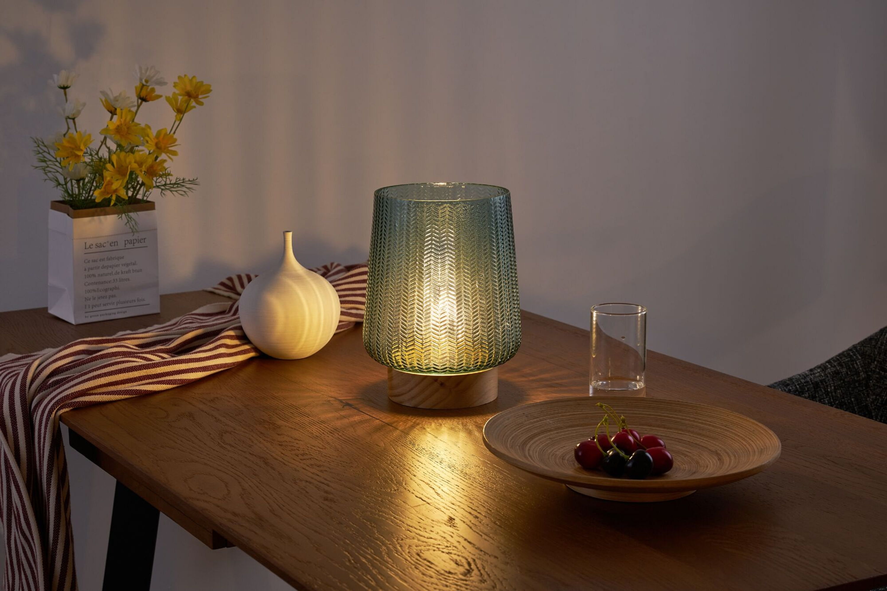 Stół z lampą, wazonem i miską wiśni. Lampa jest zapalona, tworząc ciepłą atmosferę.