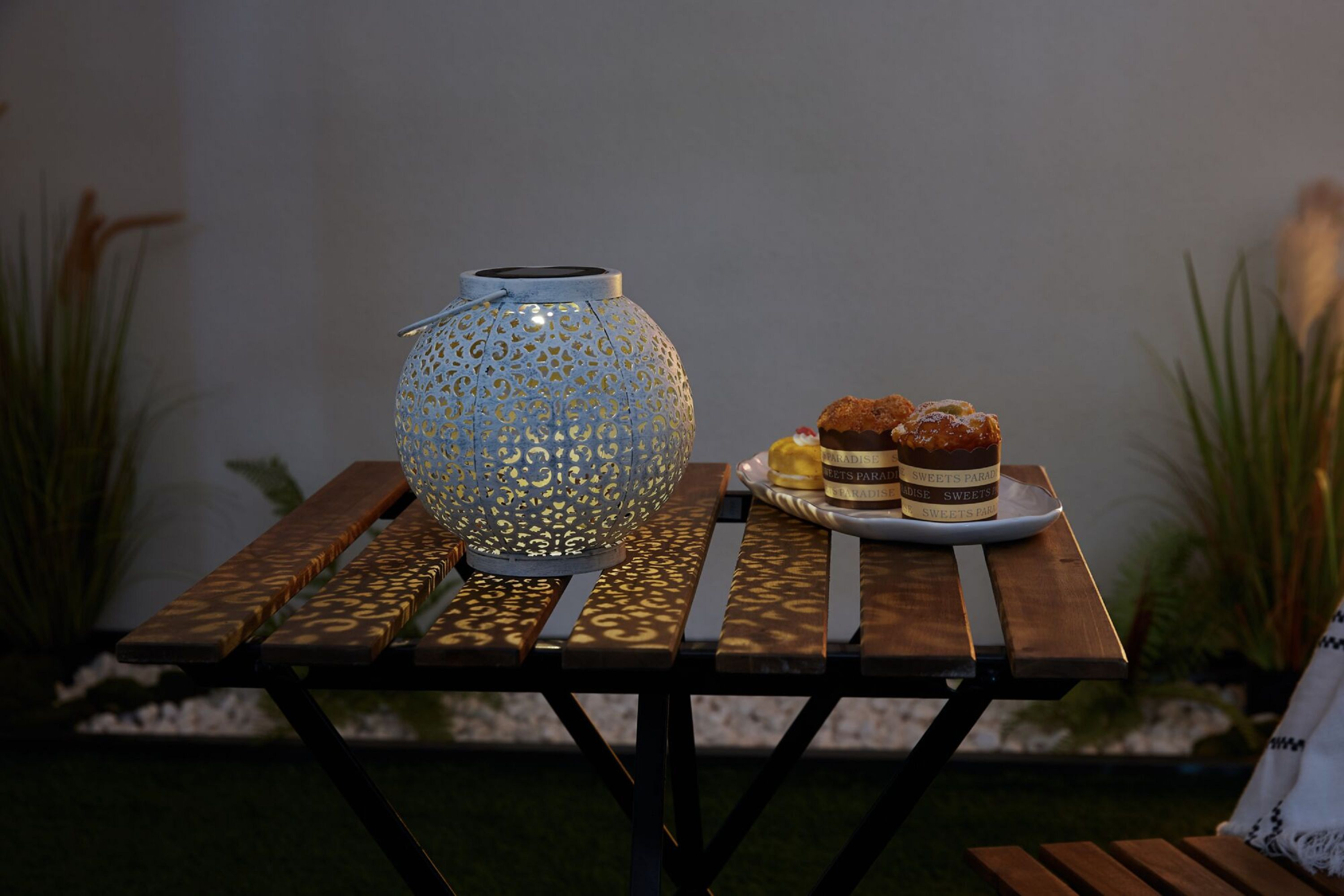 Solar-Laterne auf einem Tisch mit Kuchen. Gras und eine Wand im Hintergrund.