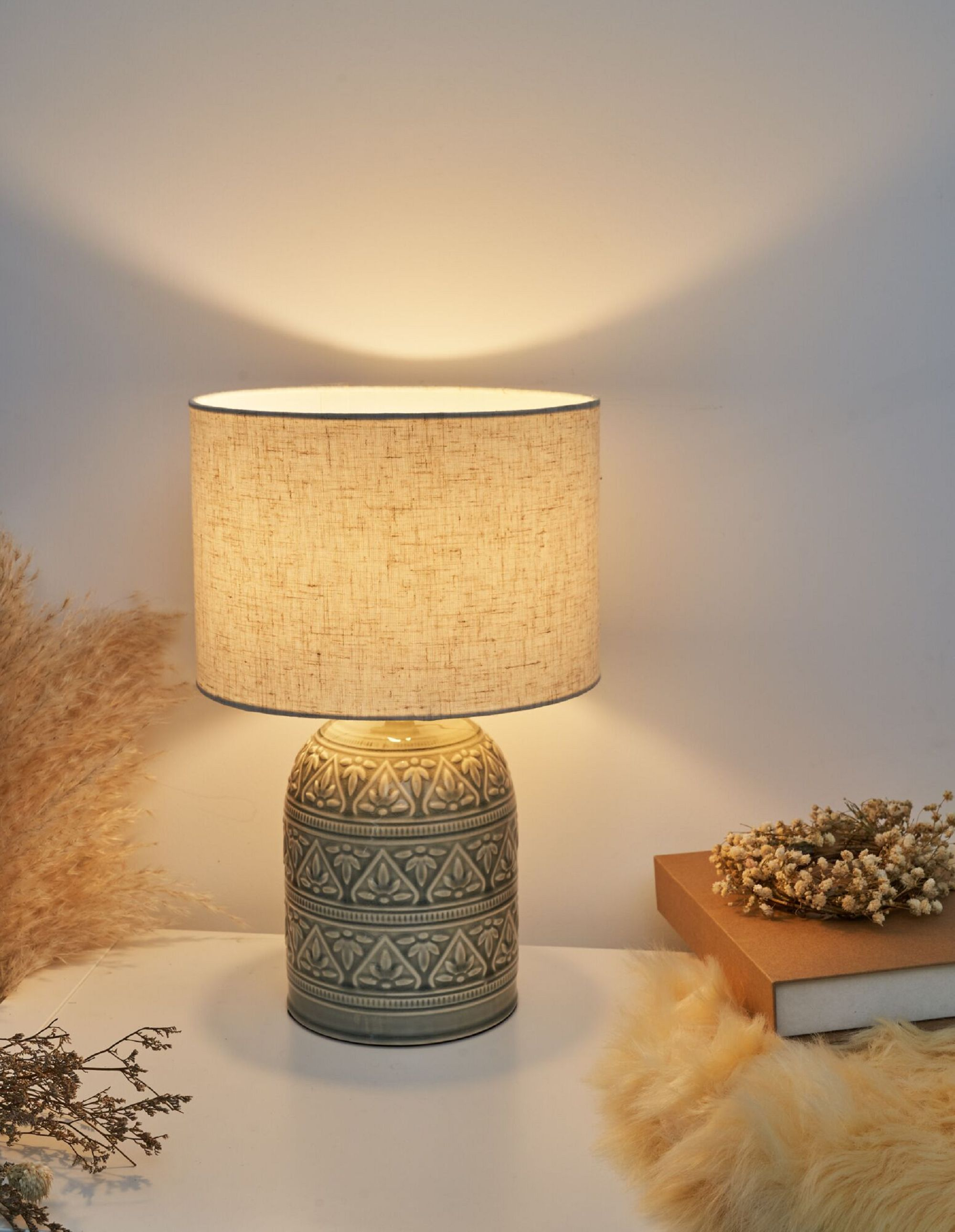 Lampa stołowa z beżowym abażurem i wzorzystą podstawą. Na stole leży książka.