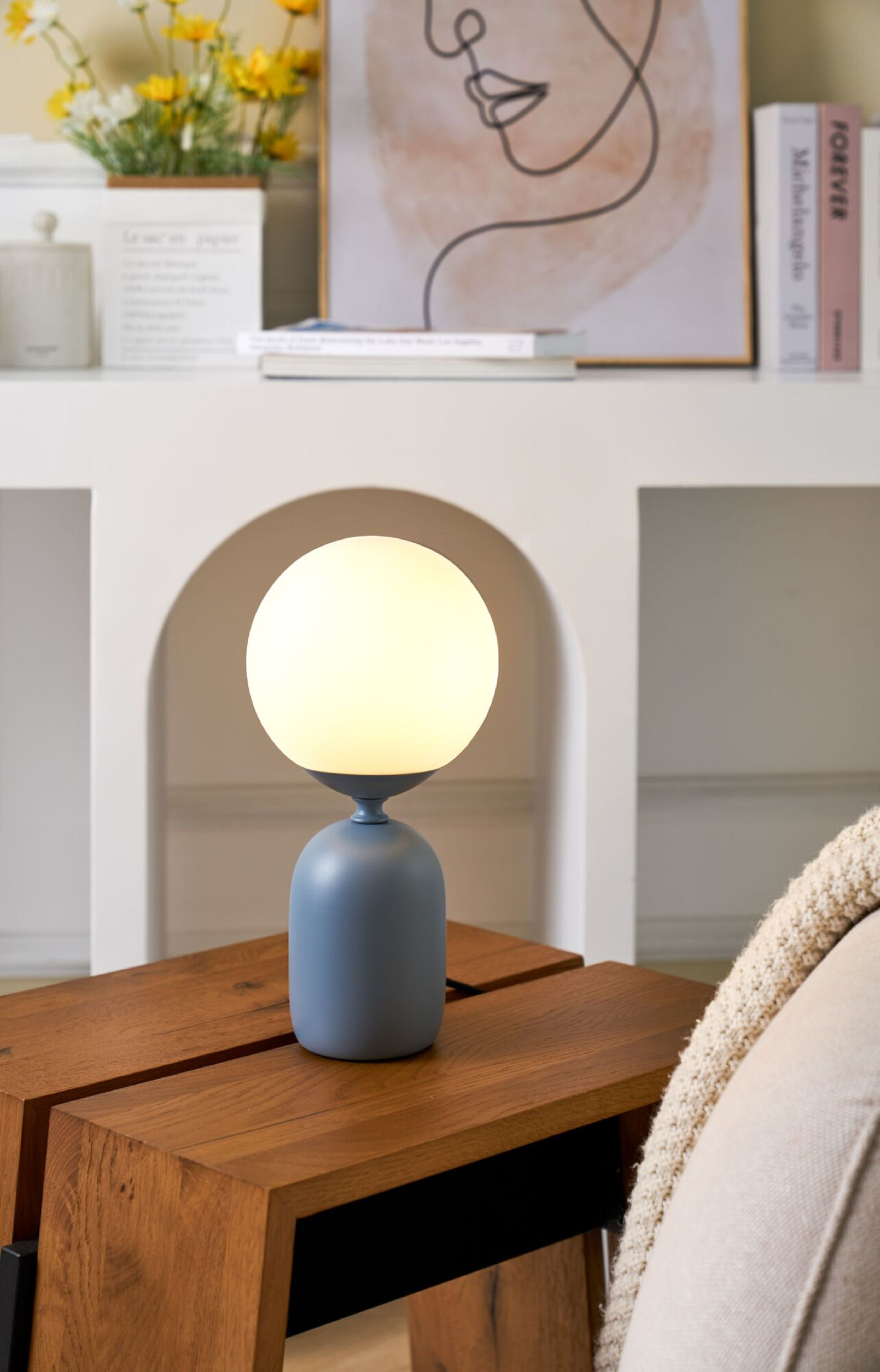 Niebiesko-biała lampa na drewnianym stole. Obraz i dekoracje w tle. Widoczna kanapa.