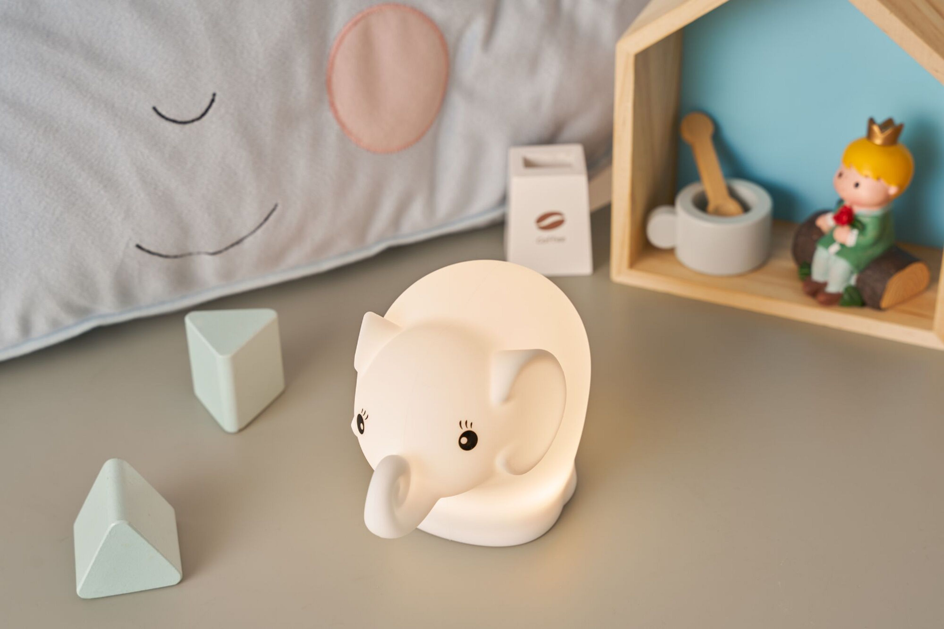 Nocna lampka w kształcie słonia i zabawki na biurku. Nocna lampka świeci.