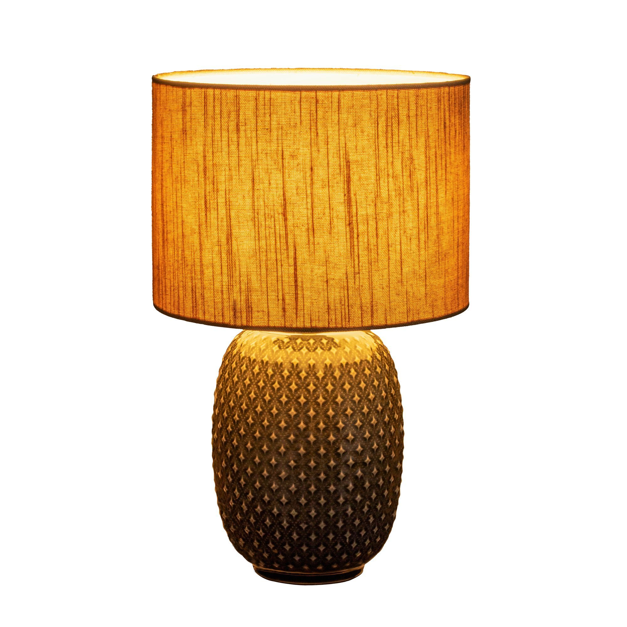 Lampa z teksturowaną podstawą i abażurem ze złotym wzorem. Lampa stoi na białej powierzchni.