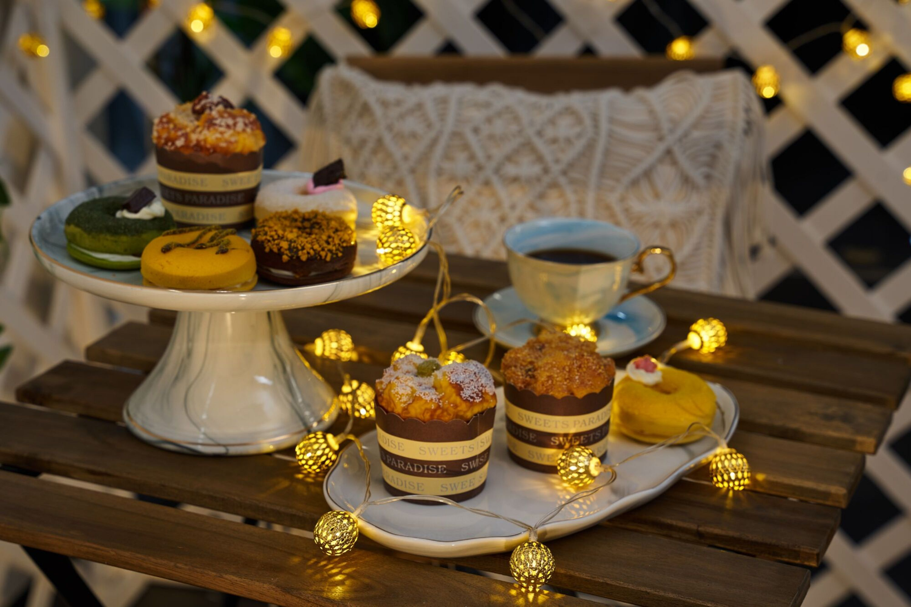 Stół z pączkami, ciastkami, filiżanką herbaty i lampkami choinkowymi.