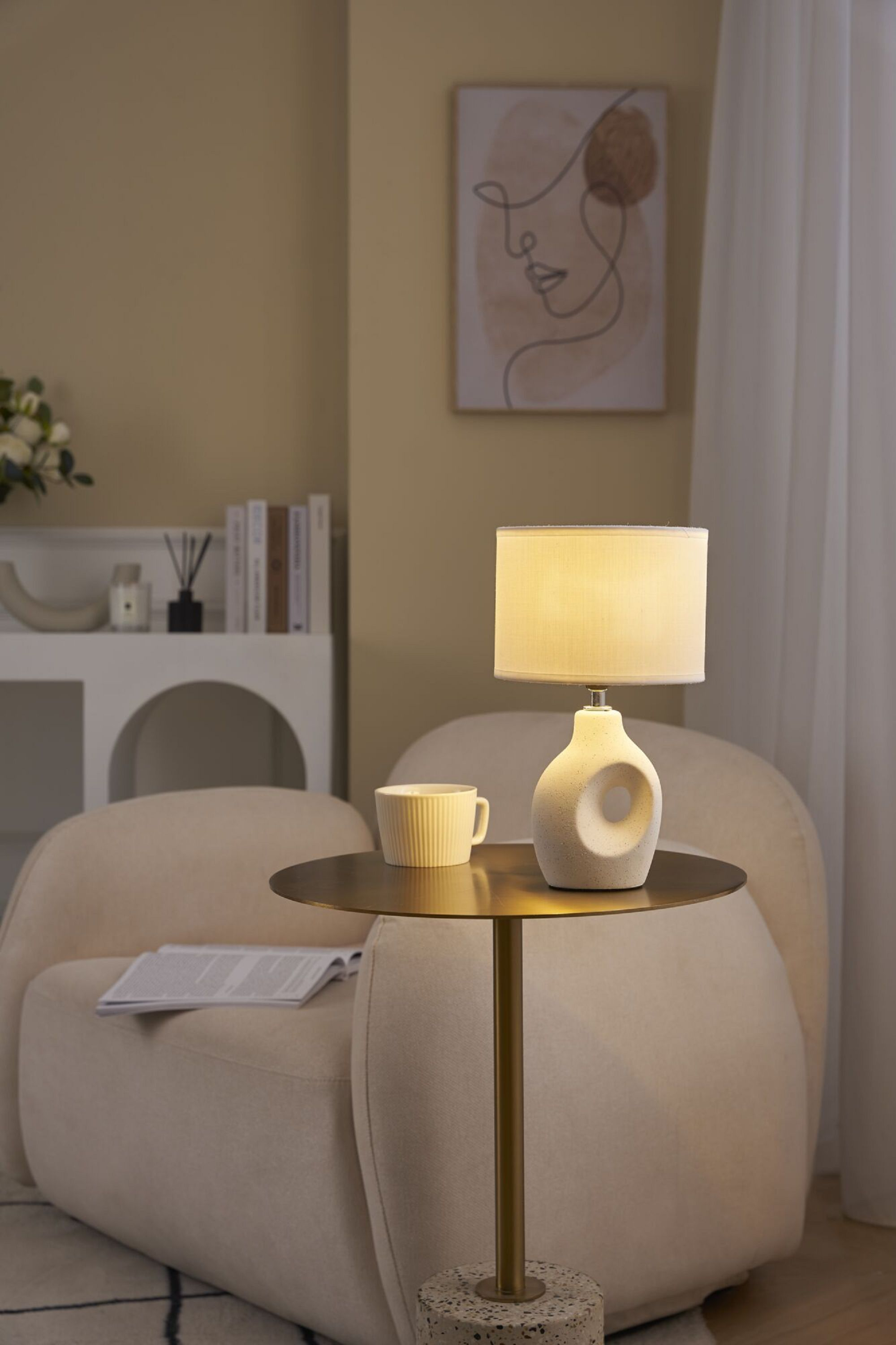 Lampa stołowa na stole z filiżanką. Krzesło i obraz w tle.