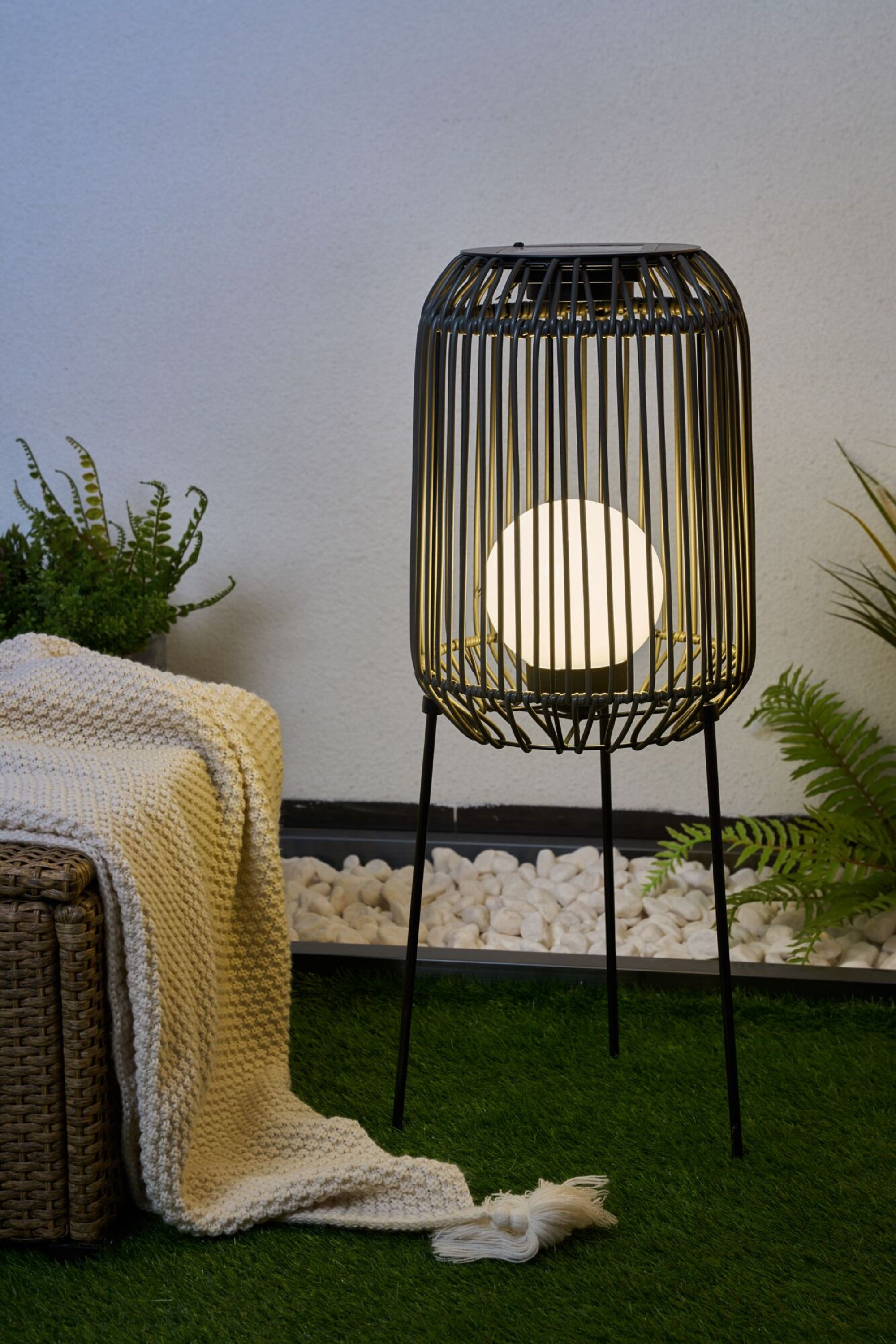 Czarna latarnia z świecącą kulą w środku, umieszczona na zielonej trawie, białe tło.