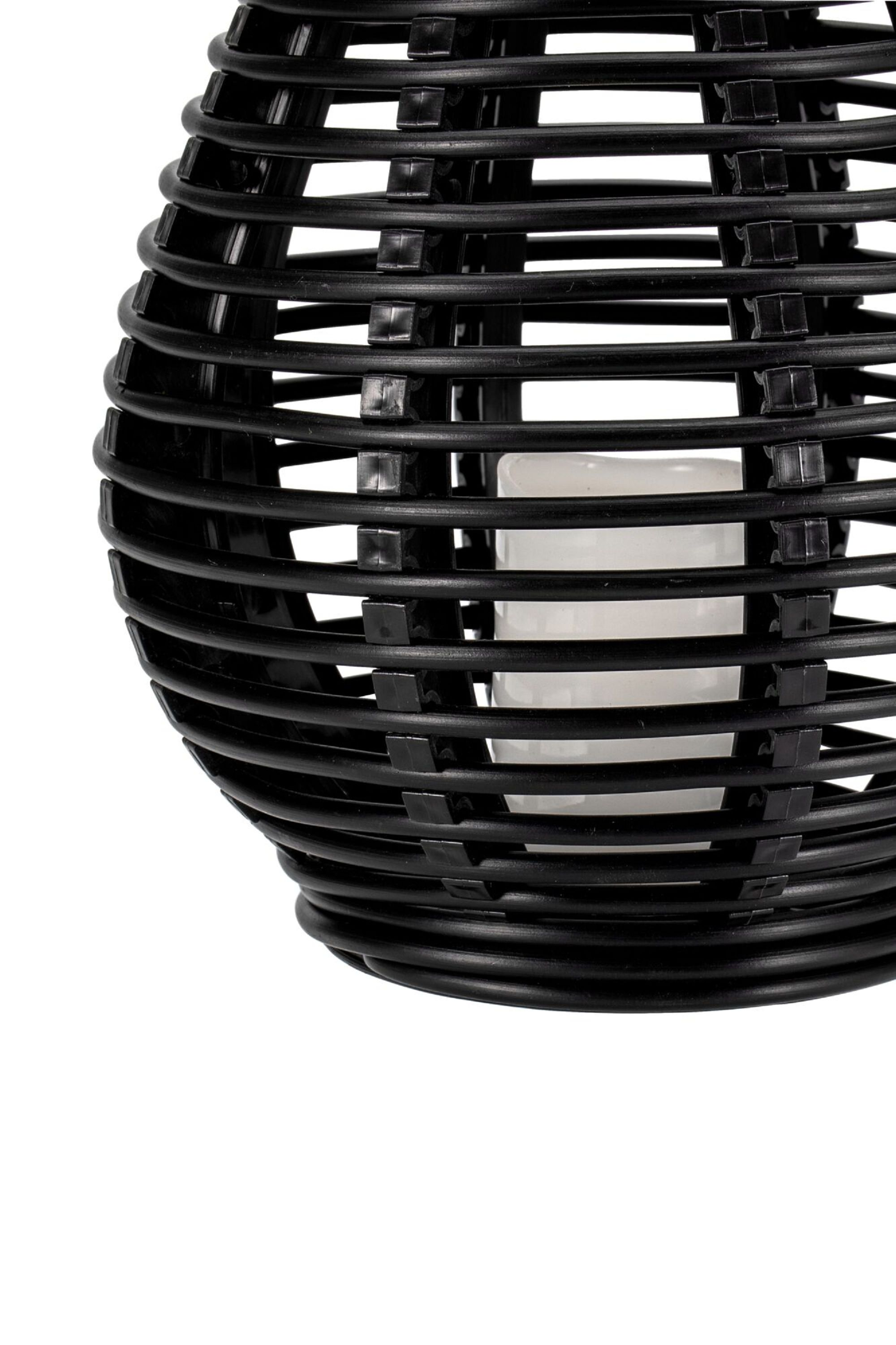 Czarna tkana latarnia. W środku ma białą świecę.