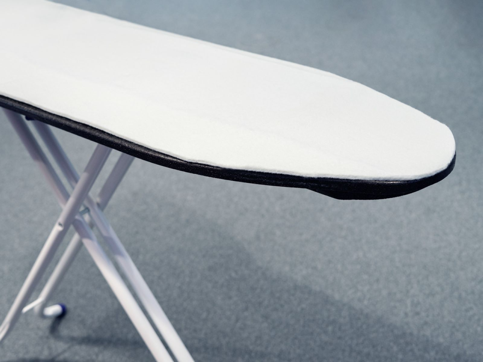 Deska do prasowania z białą, wyściełaną powierzchnią i czarną krawędzią, na białej ramie.