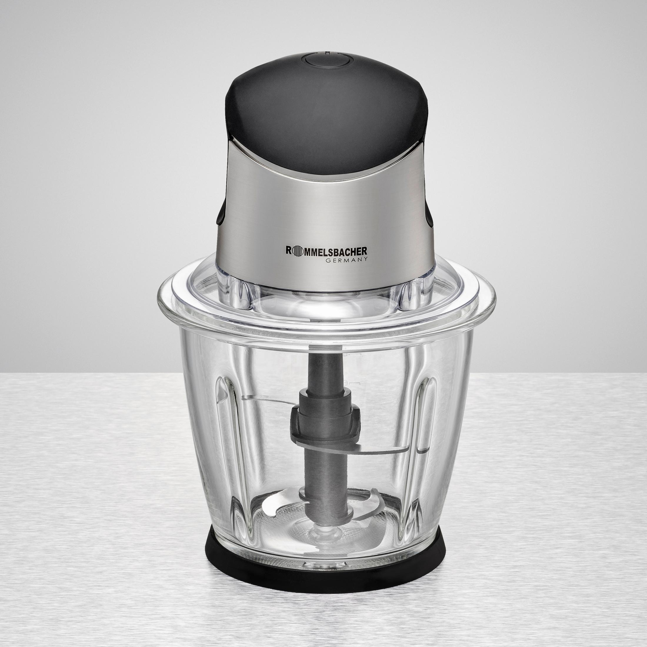 Ein silberner und schwarzer Foodprocessor mit einer durchsichtigen Glasschüssel und schwarzem Sockel. Heller Hintergrund.