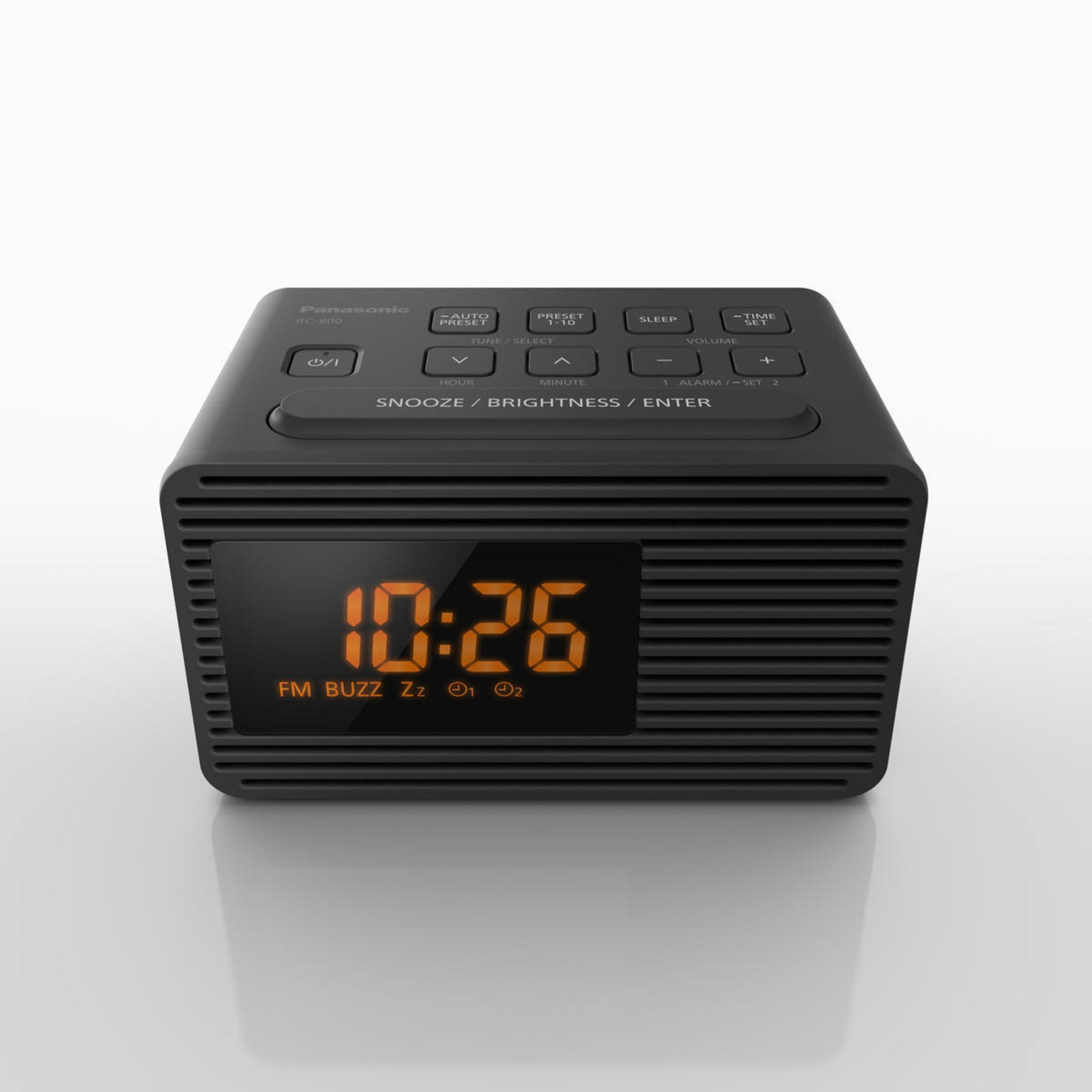 Czarny cyfrowy budzik z pomarańczowym wyświetlaczem pokazującym godzinę. Białe tło.