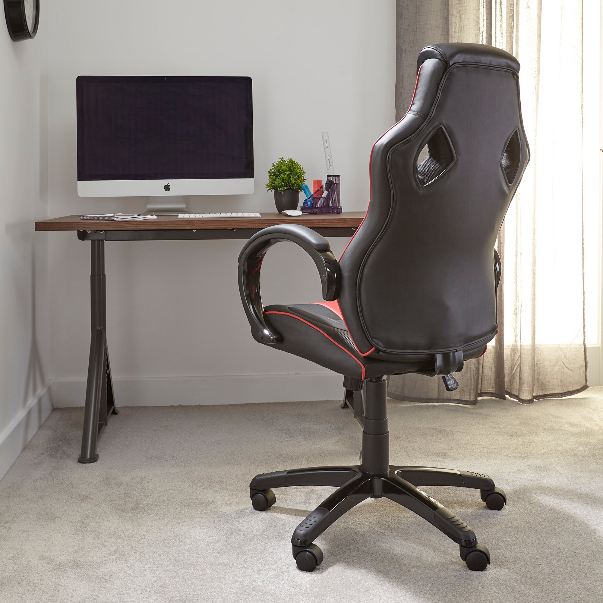 Gaming-Stuhl, Schreibtisch und Computer in einem Raum. Der Stuhl ist schwarz und rot.