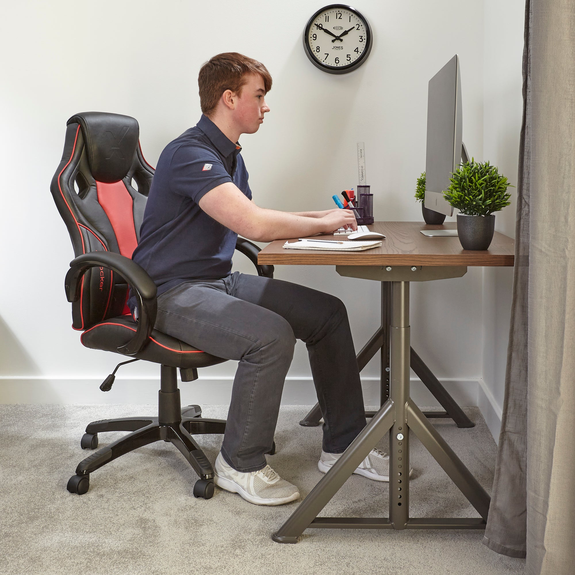 Mann sitzt an einem Schreibtisch und arbeitet an einem Computer. Eine Uhr hängt an der Wand.