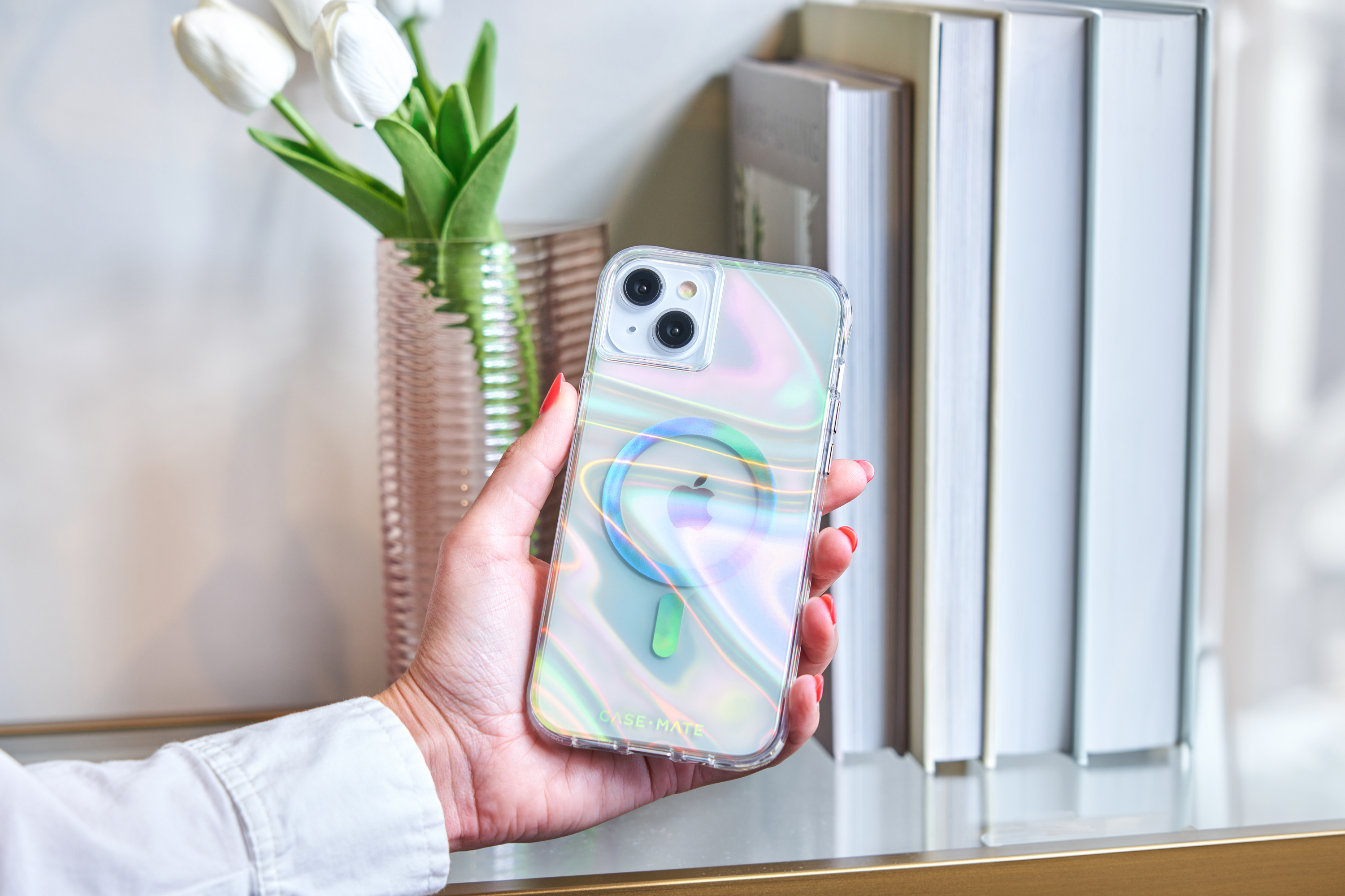 Mano che tiene uno smartphone in una custodia trasparente iridescente, logo Apple visibile.