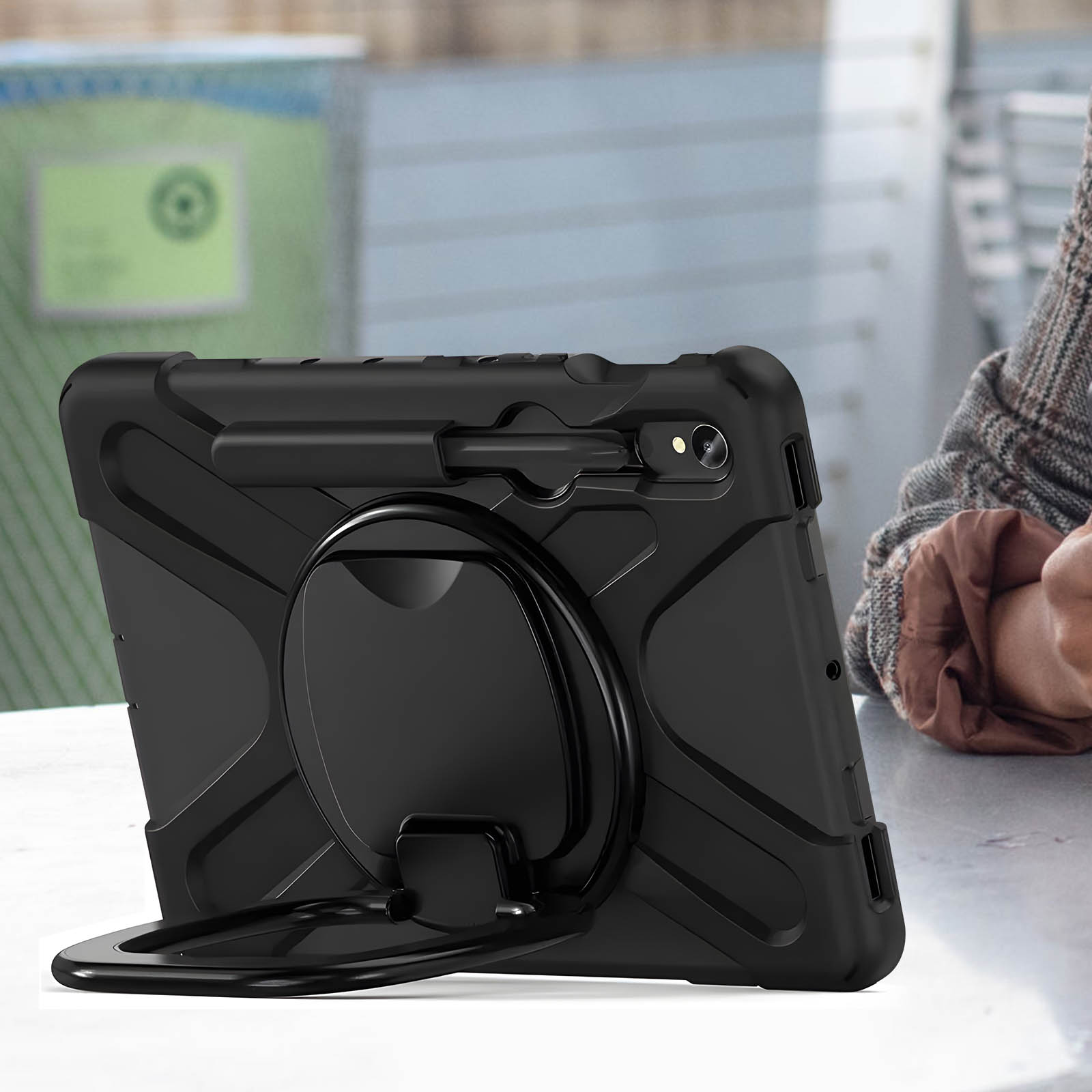 Schwarze Tablet-Hülle mit Ständer, auf einem Tisch in der Nähe einer Person.