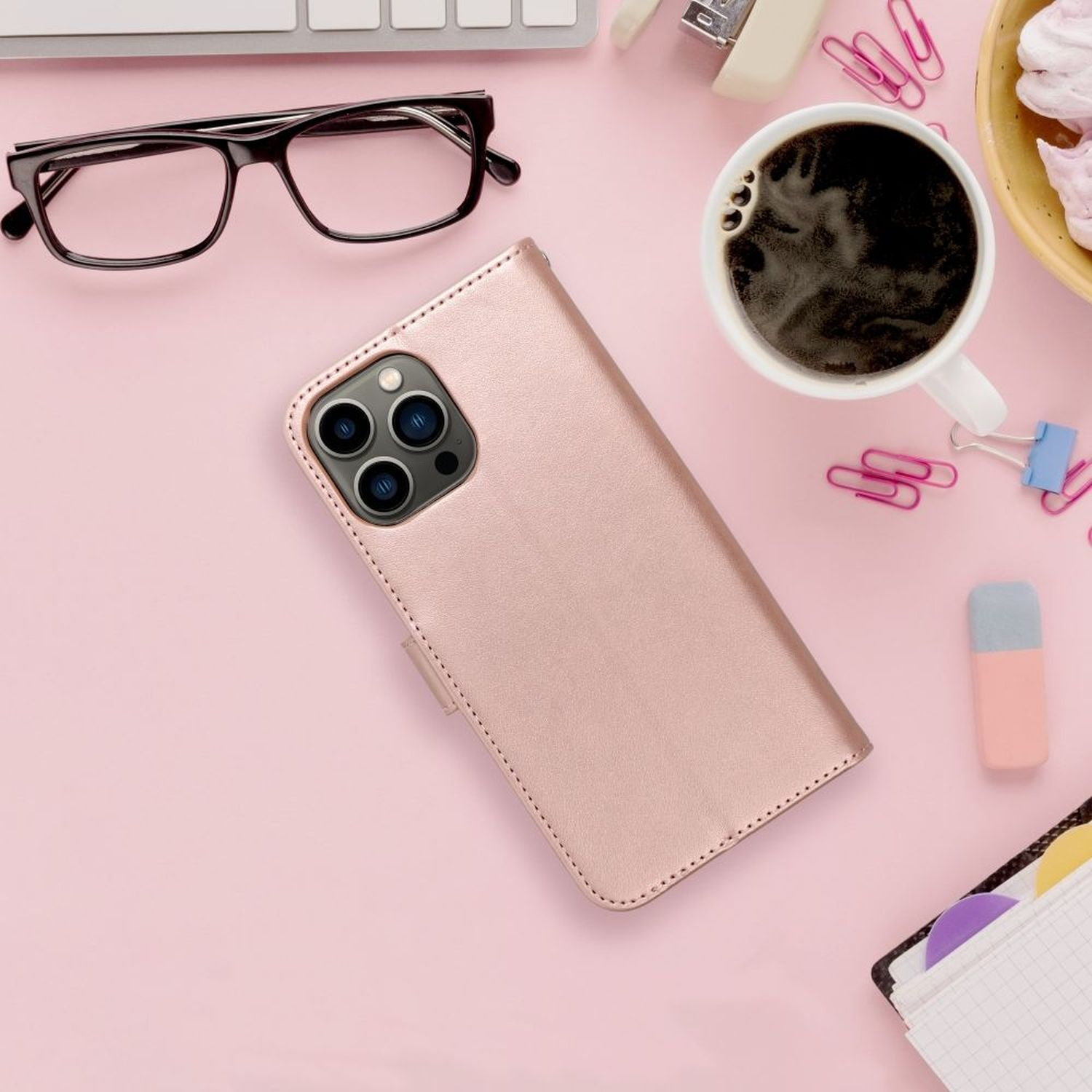 Rosa Schreibtisch mit Telefon in roségoldener Hülle, Kaffee, Brille, Radiergummi und Büroklammern.