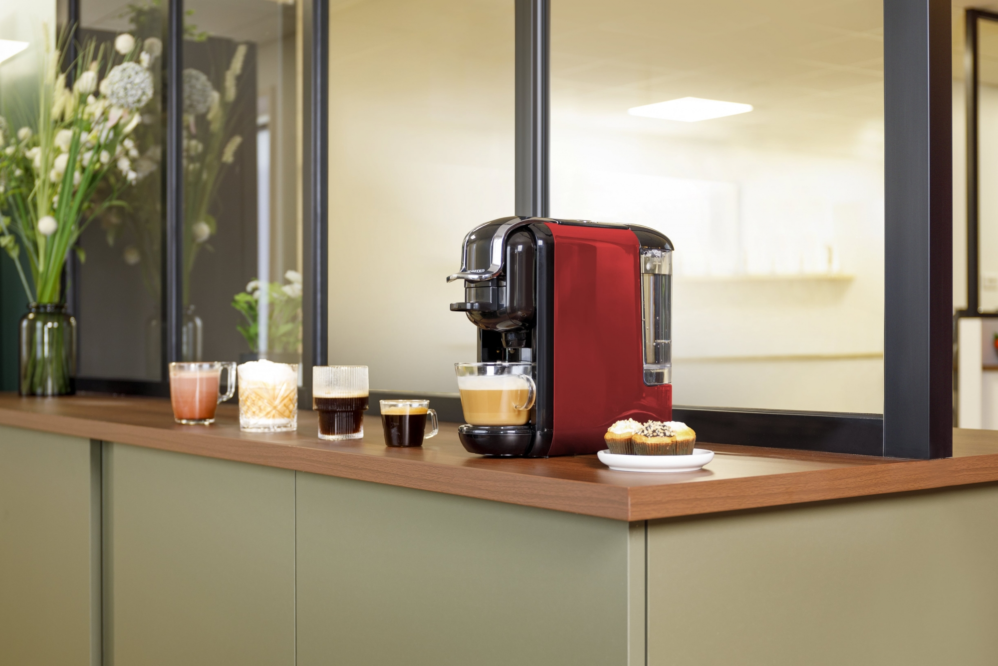 Macchina del caffè con tazze di caffè e muffin su un bancone.