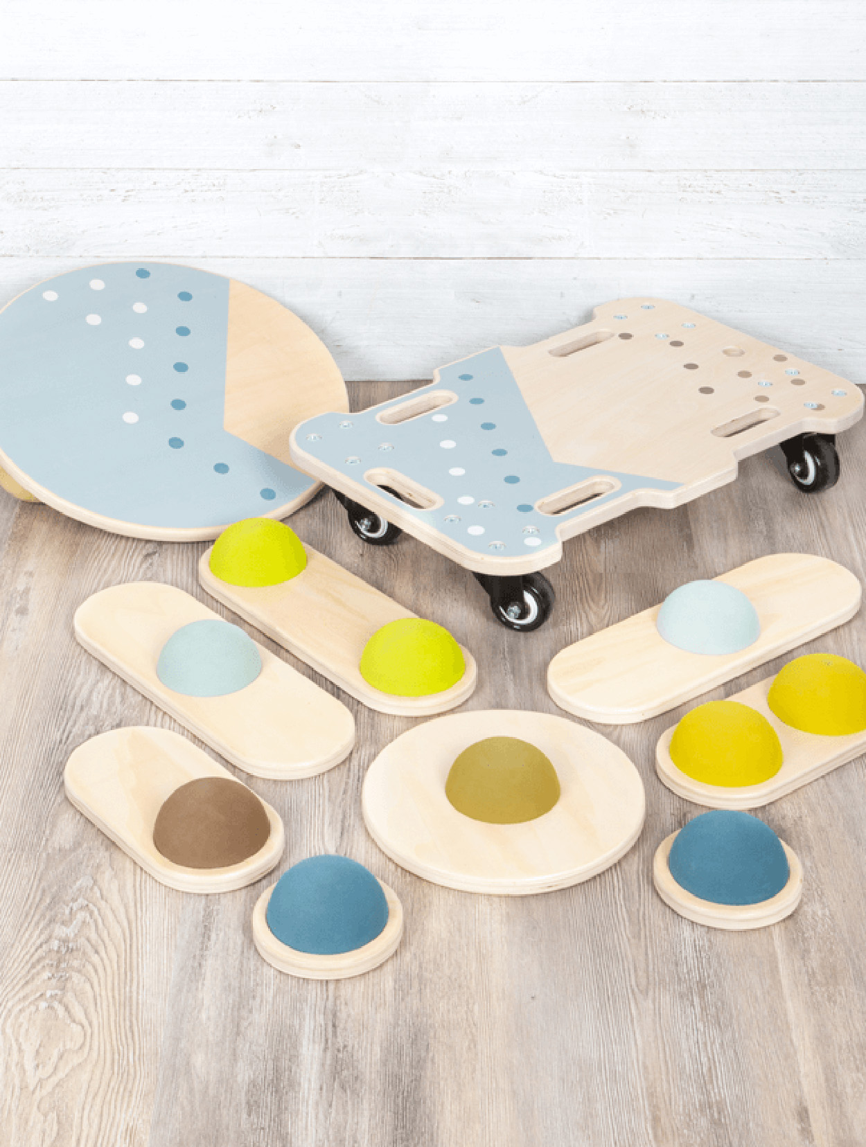 Holz-Balance Board und verschiedene Balance-Spielzeuge in Pastellfarben, auf Holzfußboden angeordnet.