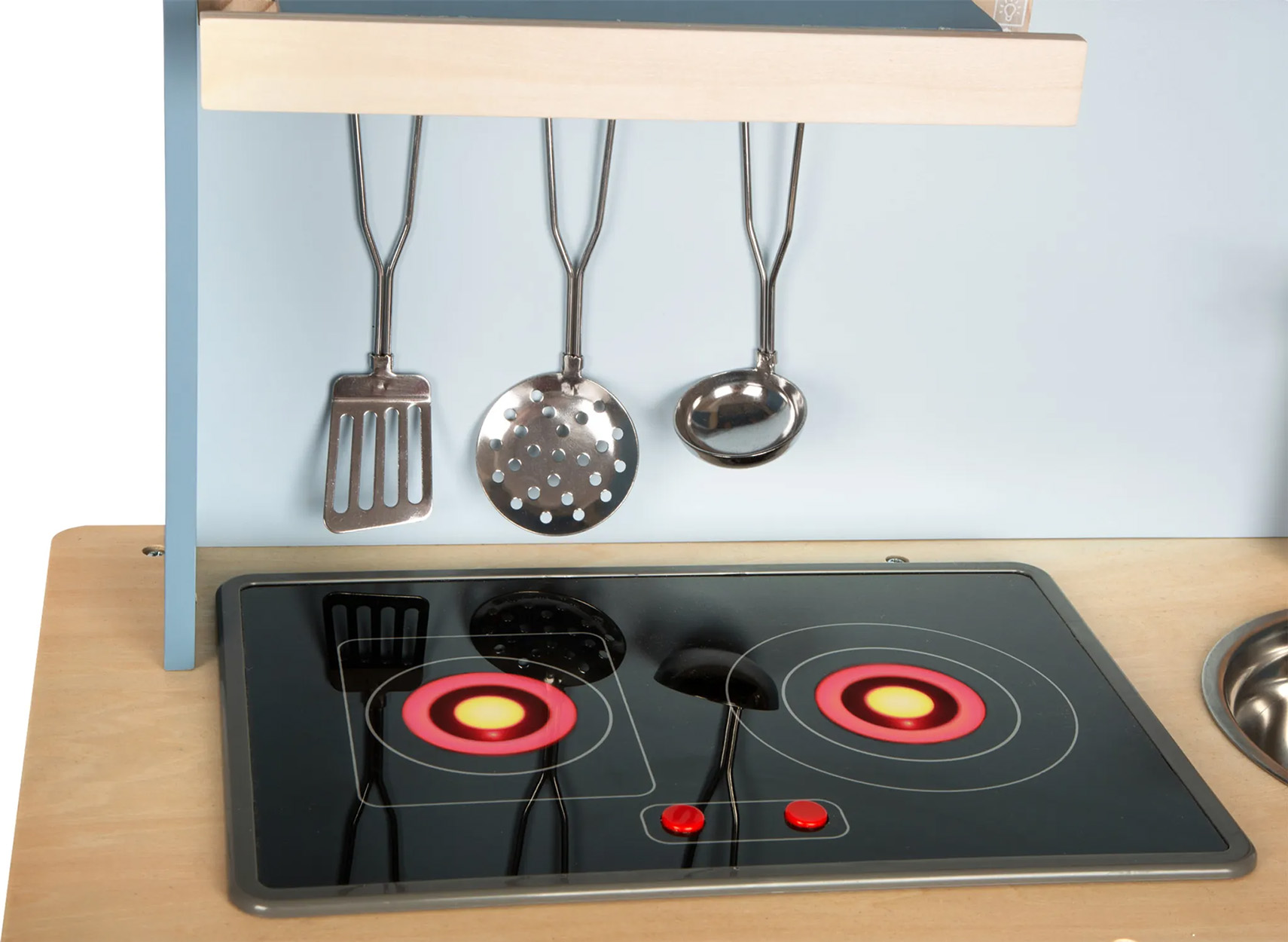 Spielzeugküche mit Herd, Utensilien und hellblauem Hintergrund.