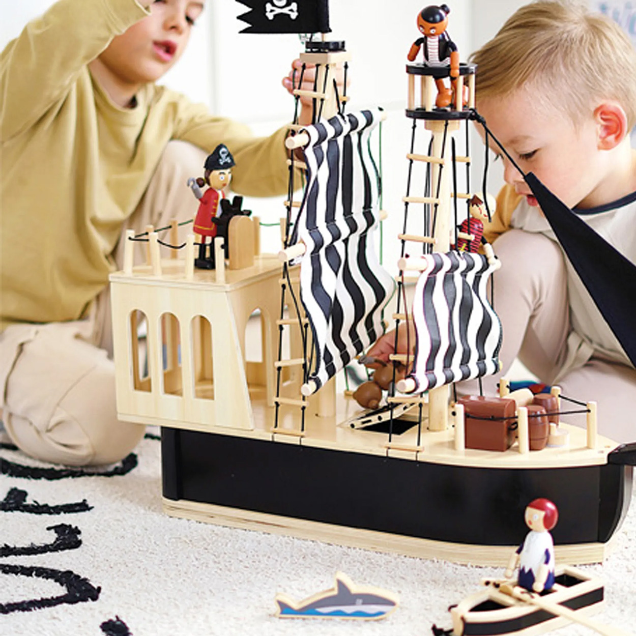 Bambini che giocano con una nave pirata giocattolo. La nave ha vele, figure e uno squalo.