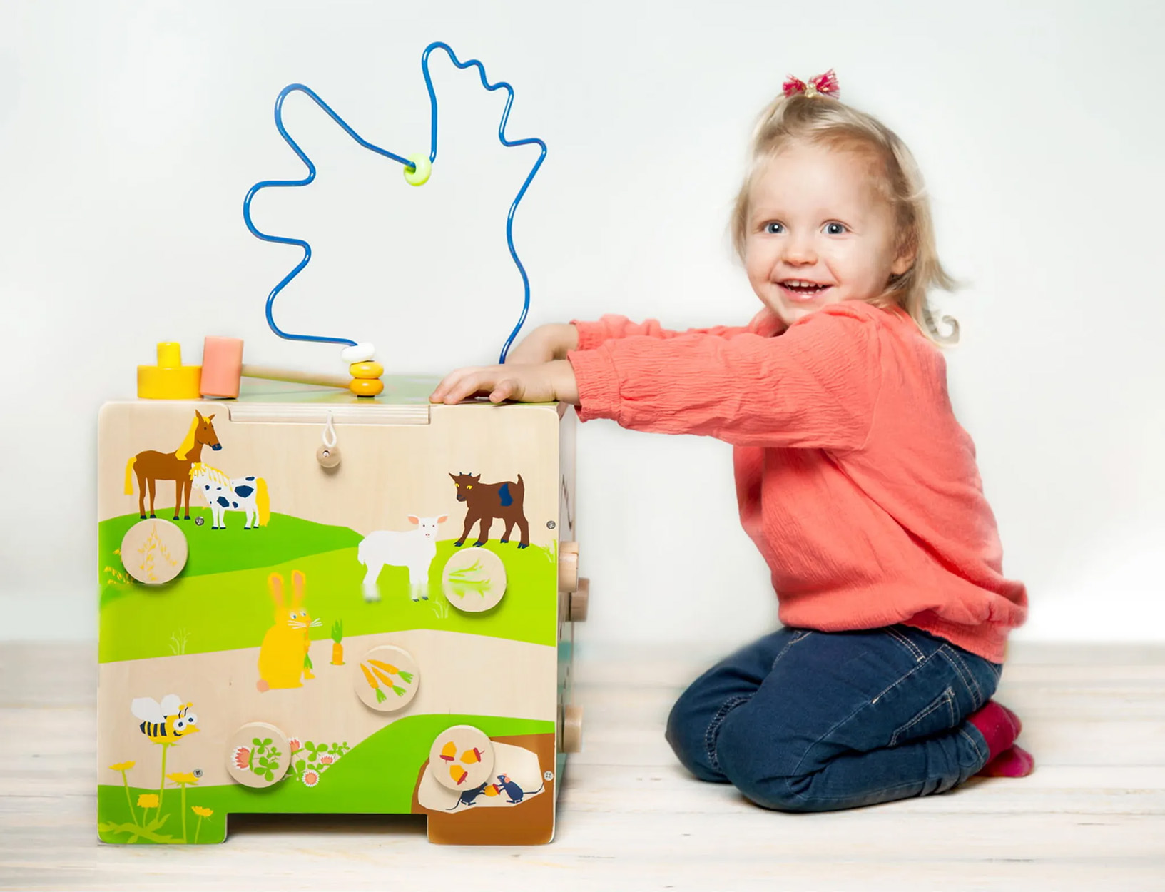 Ein junges Mädchen spielt mit einem Holzspielzeug mit Labyrinth und Tierfiguren, lächelt in die Kamera.