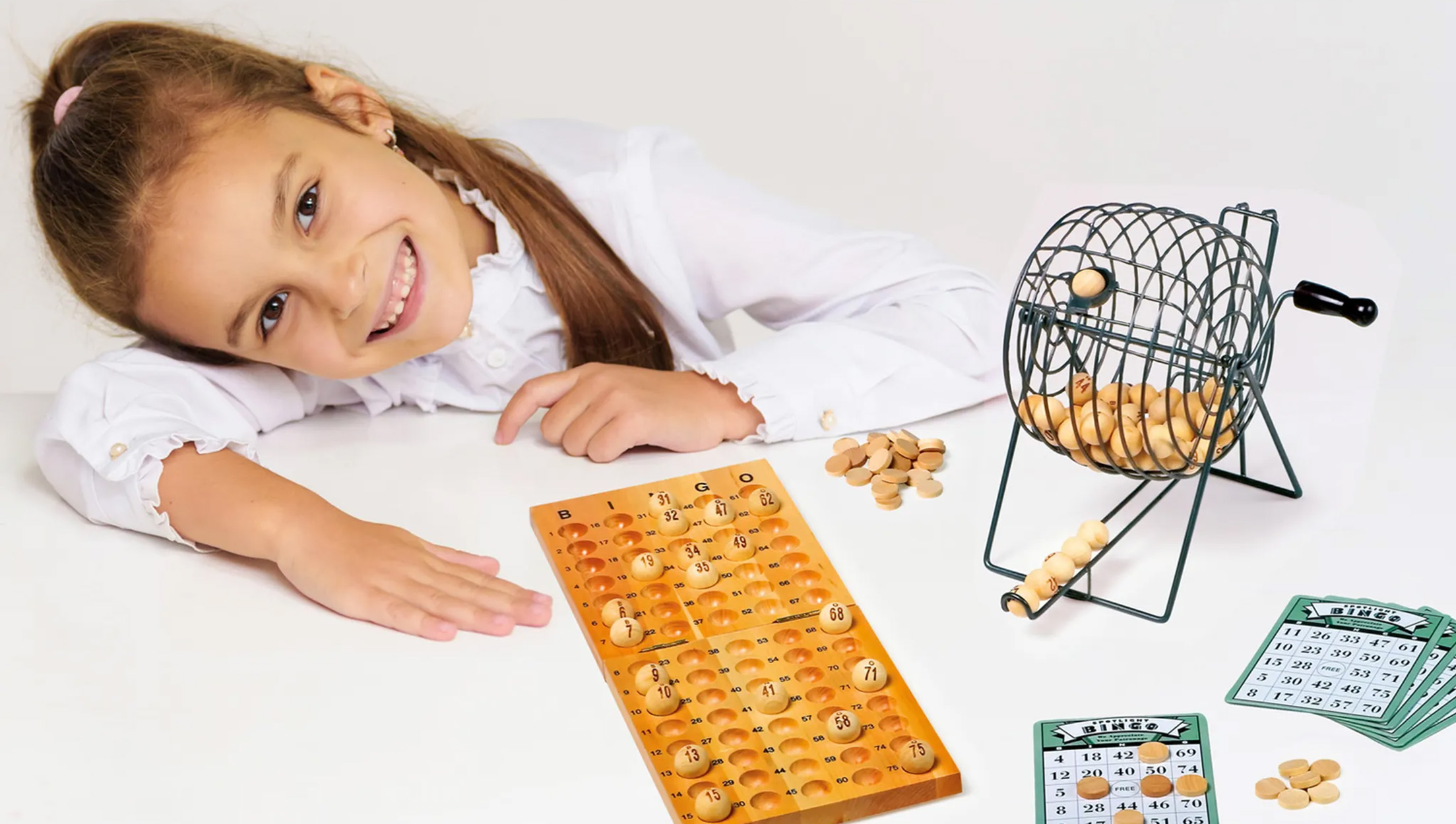 Ein Mädchen lächelt in die Kamera, während sie Bingo mit einem Holzbrett, Spielsteinen und einer Trommel spielt.
