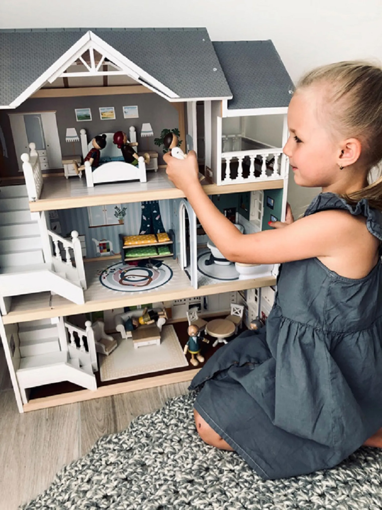 Ein Mädchen spielt mit einem Puppenhaus. Es hat mehrere Zimmer mit Möbeln.