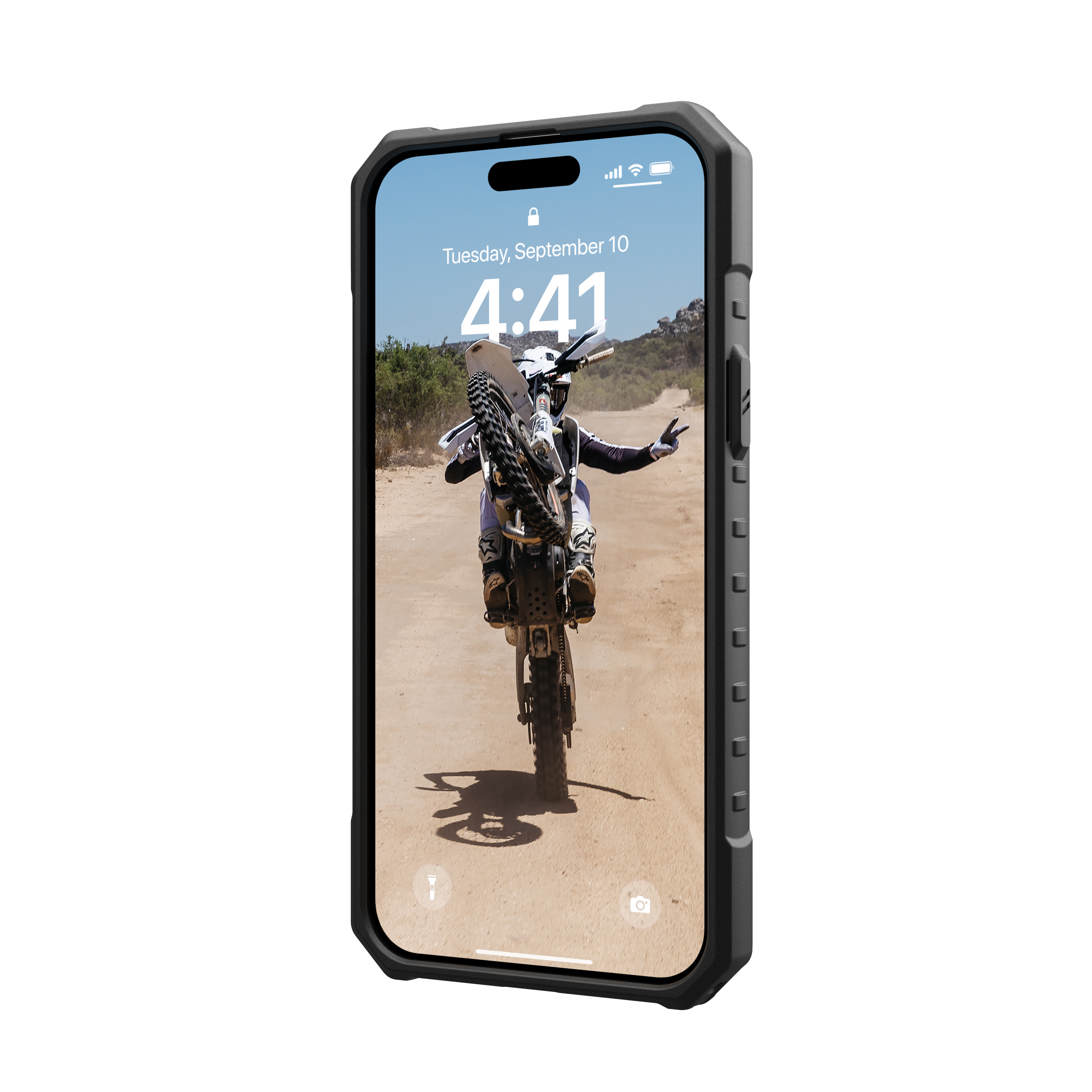 Una pantalla de teléfono muestra a una persona en una motocicleta haciendo un caballito en un camino de tierra.