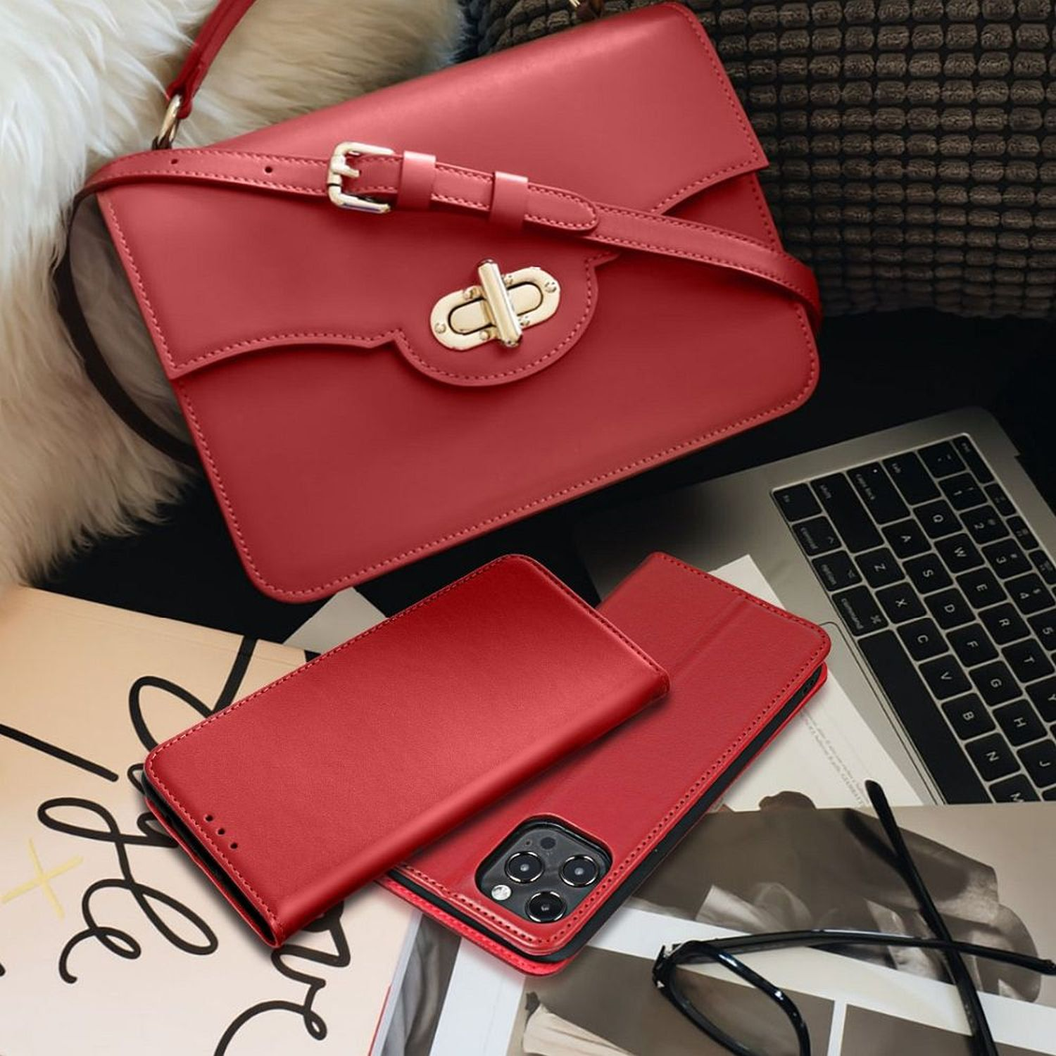 Rote Handtasche und Handyhülle mit Laptop und Brille auf einem Tisch mit Zeitschrift.
