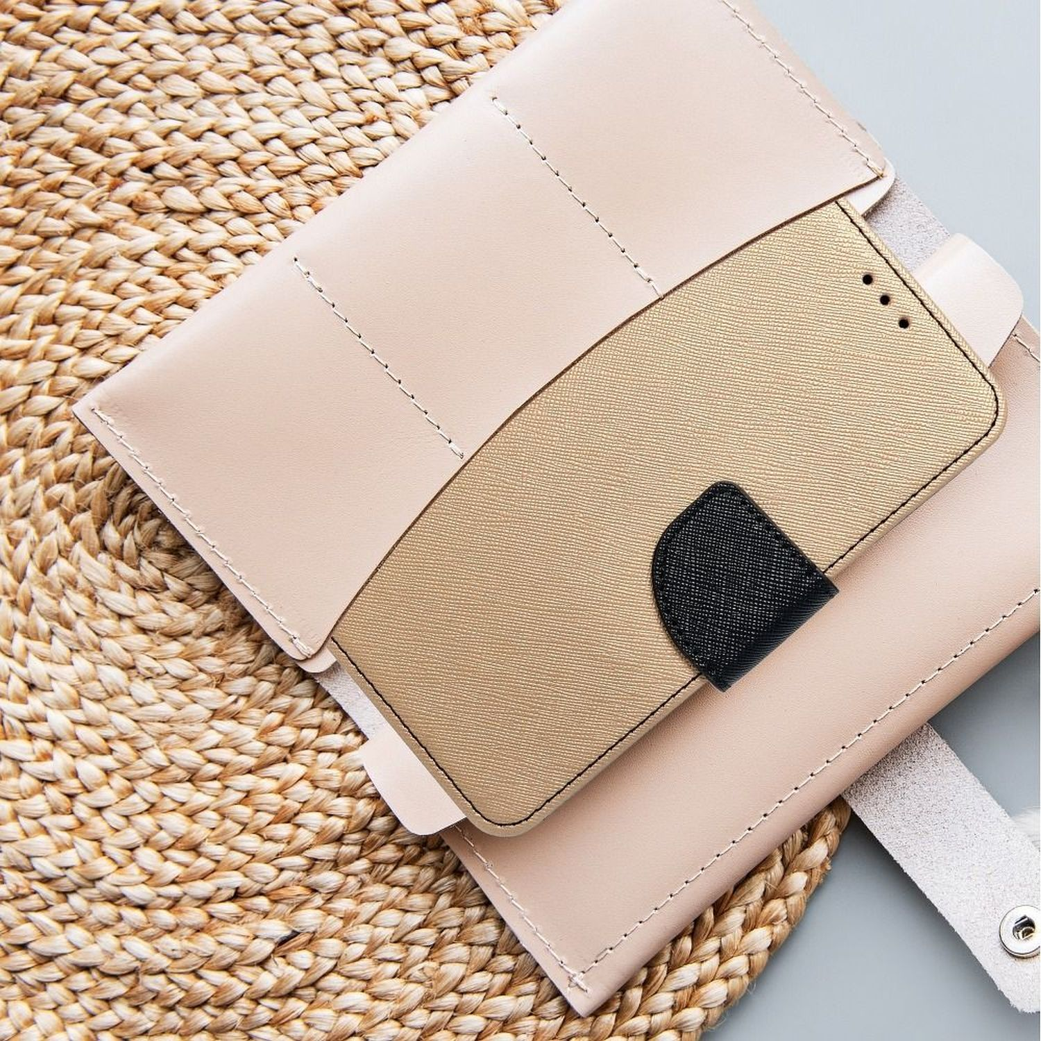 Beige Handyhülle mit goldenem Handy, auf einer gewebten Strohmatte.
