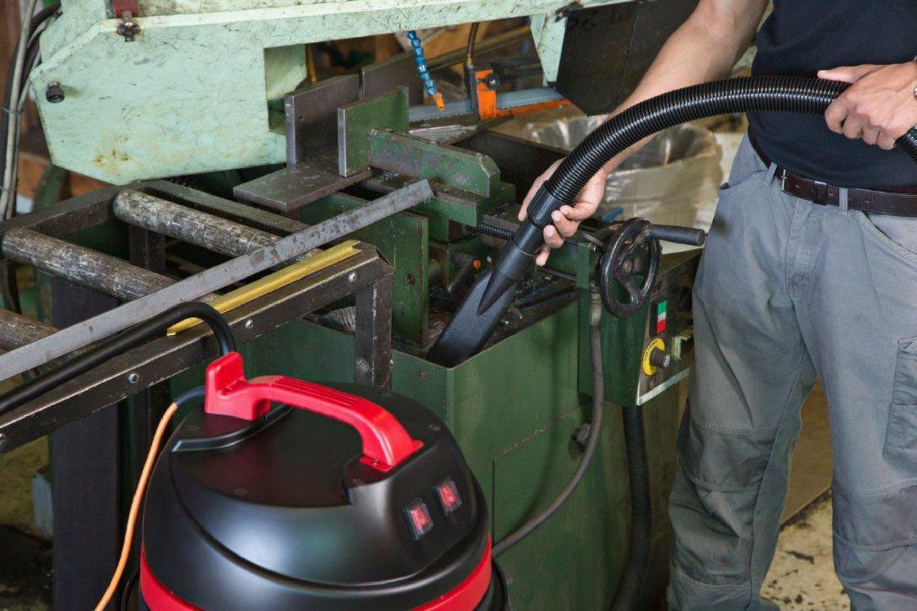 Una persona che aspira una macchina in un'officina. È visibile un aspirapolvere rosso e nero.