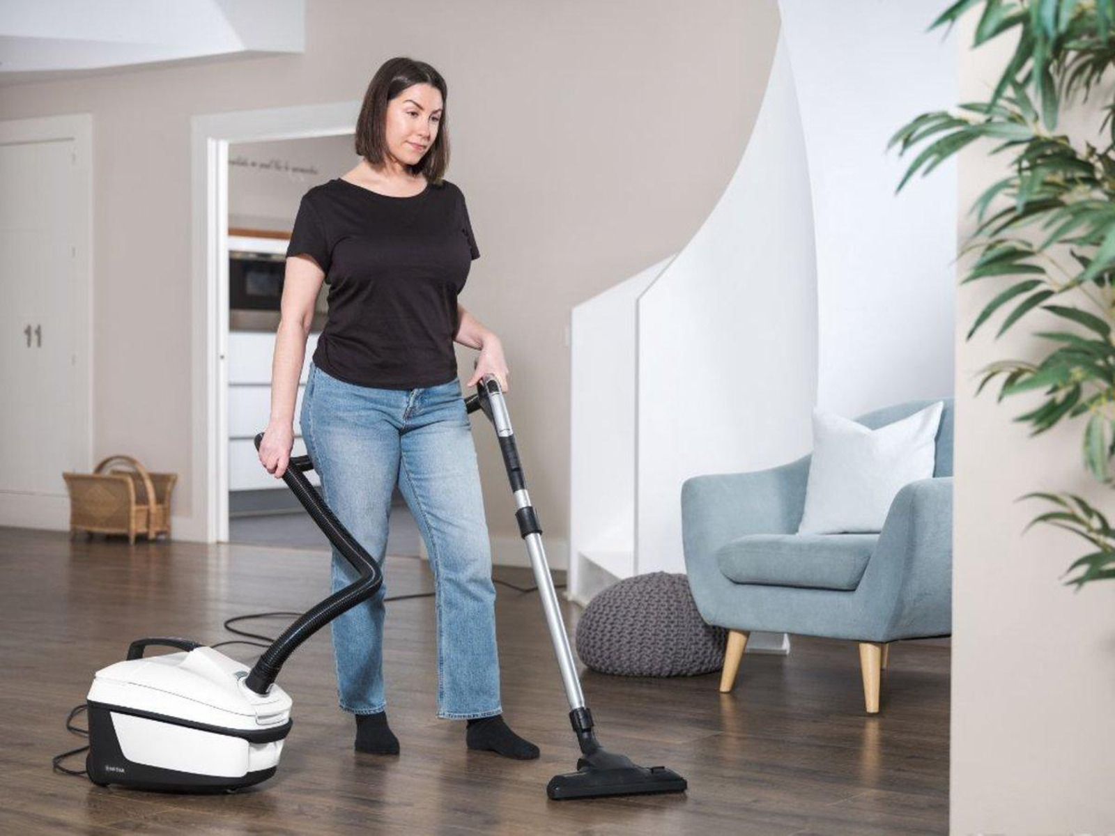 Mujer aspirando un suelo de madera en un salón.