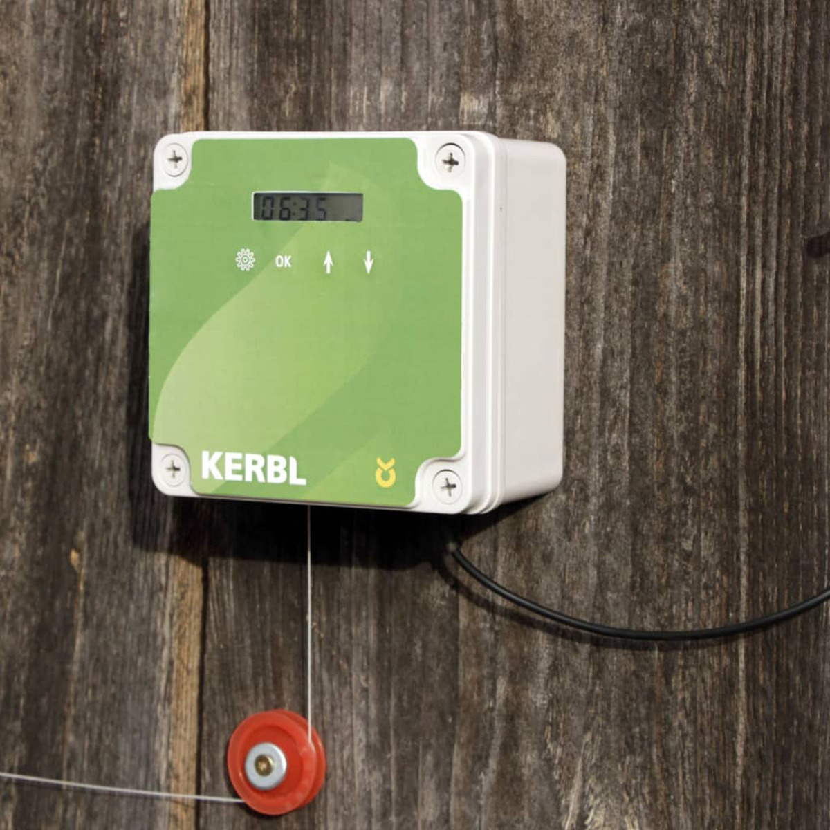 Ein weißes und grünes Gerät an einer Holzwand befestigt. Es zeigt eine Digitalanzeige mit Zahlen und Pfeilen.