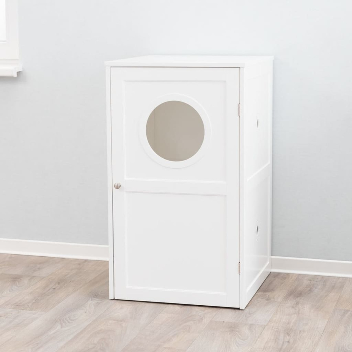 Un armario blanco para arenero con una abertura redonda en la puerta. Piso de madera clara.