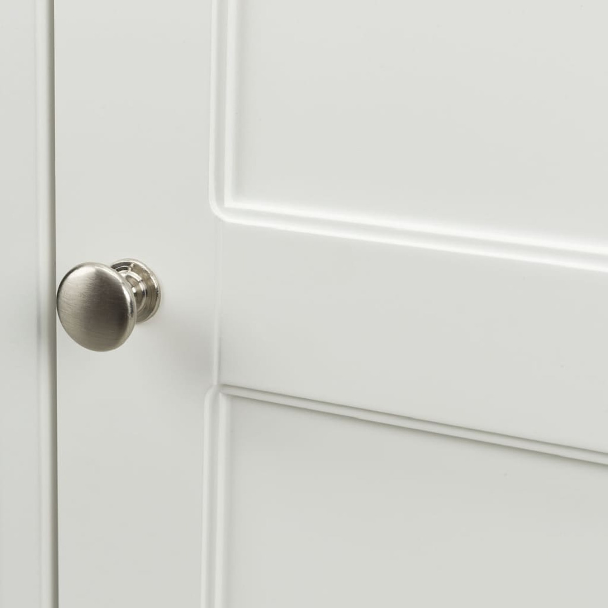 Primer plano de un pomo de puerta de metal cepillado en un armario blanco.