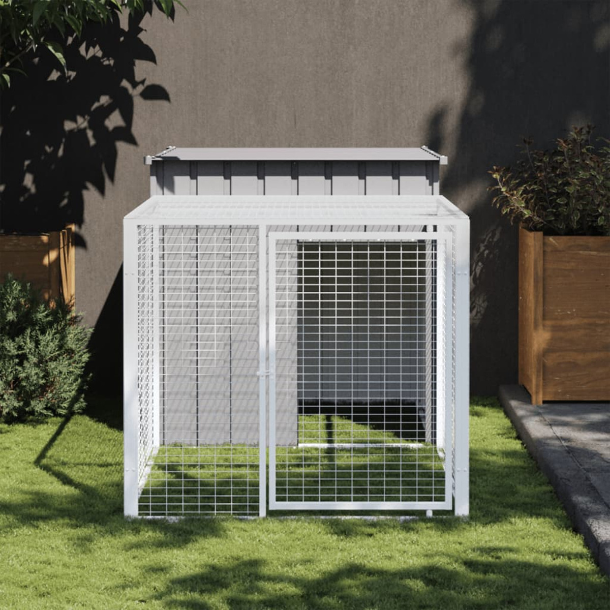 Eine Hundehütte aus weißem Metall auf grünem Gras. Sie hat eine Tür und ein Dach. Grauer Wandhintergrund.