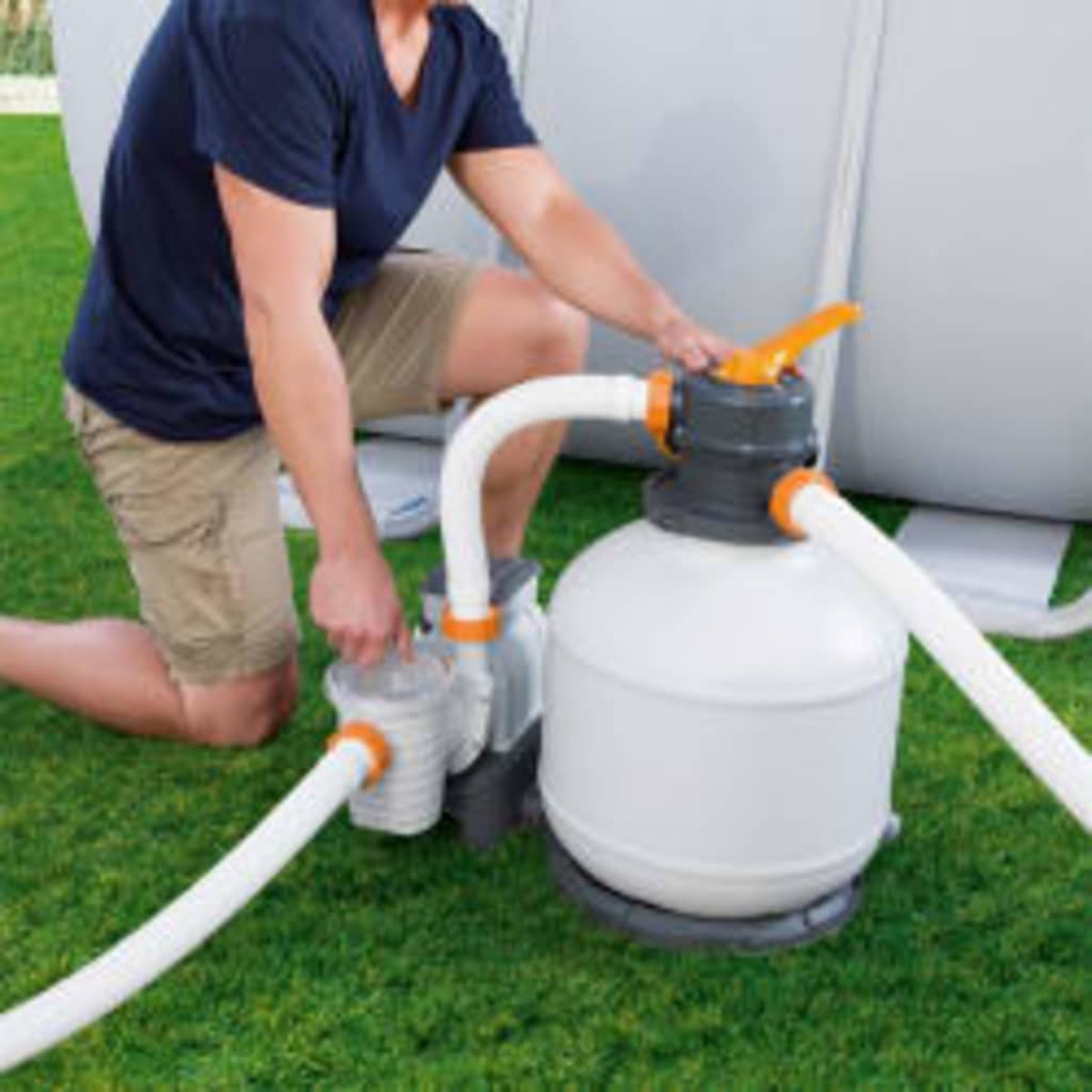 Man using a white and orange pool filter on green grass. There are white hoses.