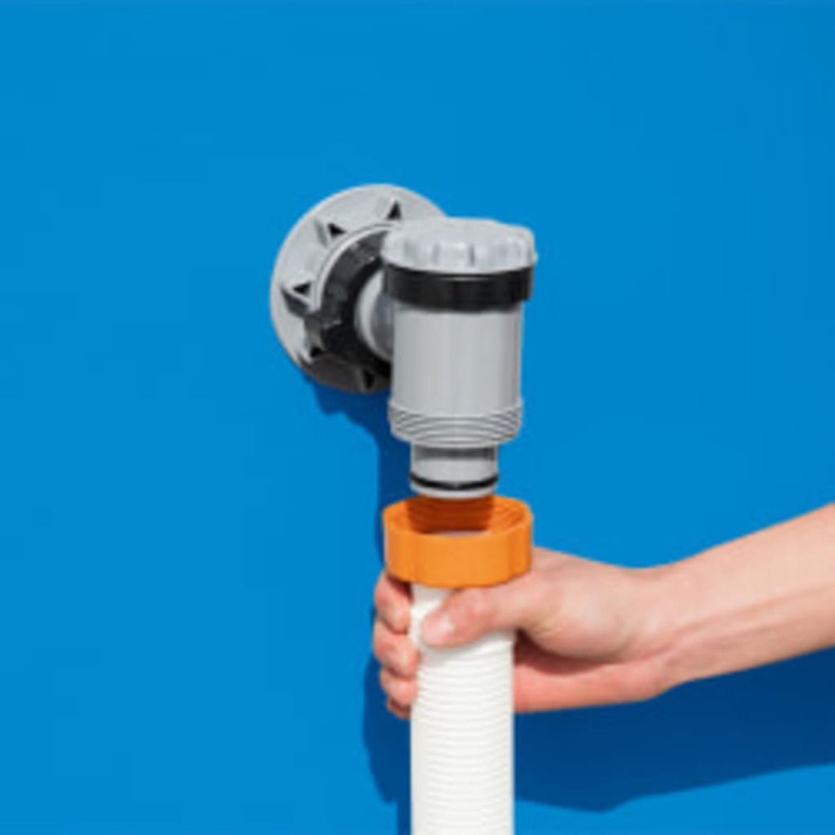 A hand holding a white hose connected to a pool wall fitting against a blue background.