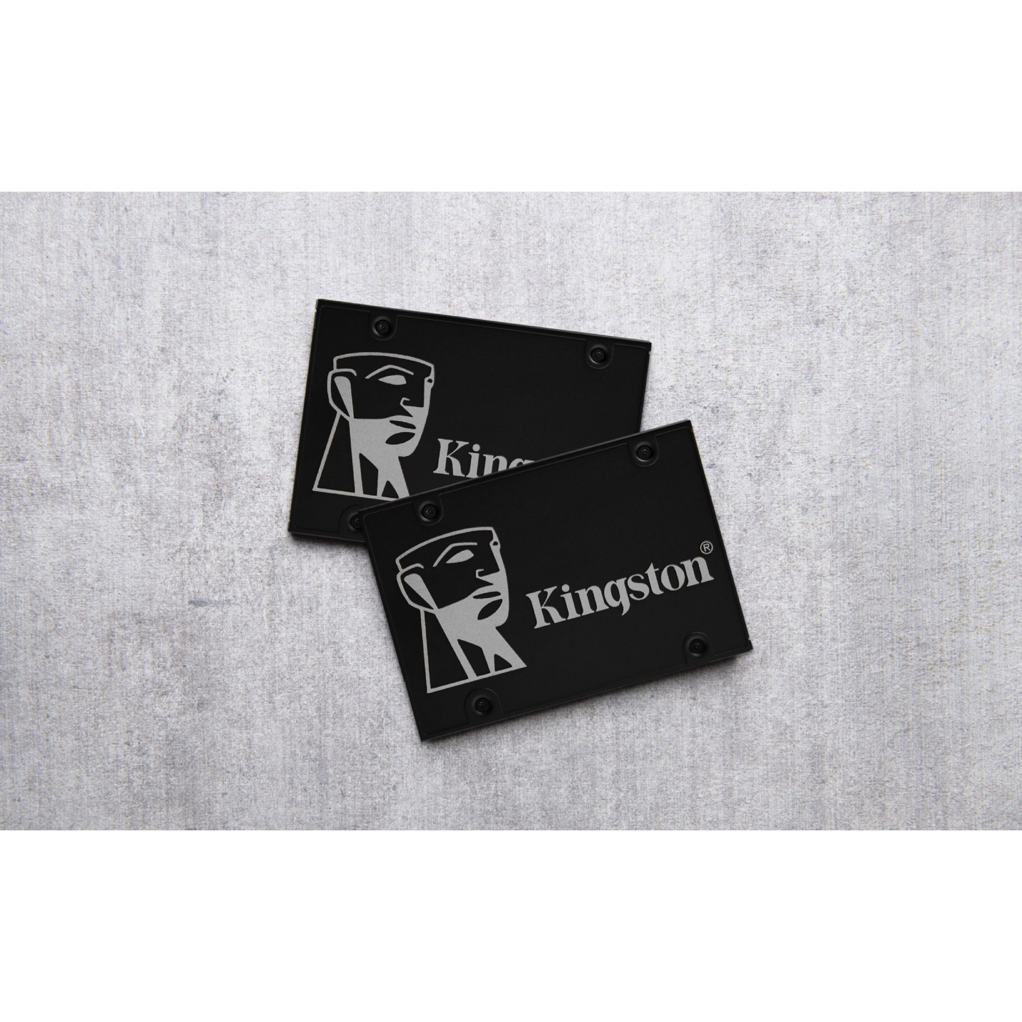 Dwa czarne dyski SSD Kingston na teksturowanej szarej powierzchni. Widok z góry.