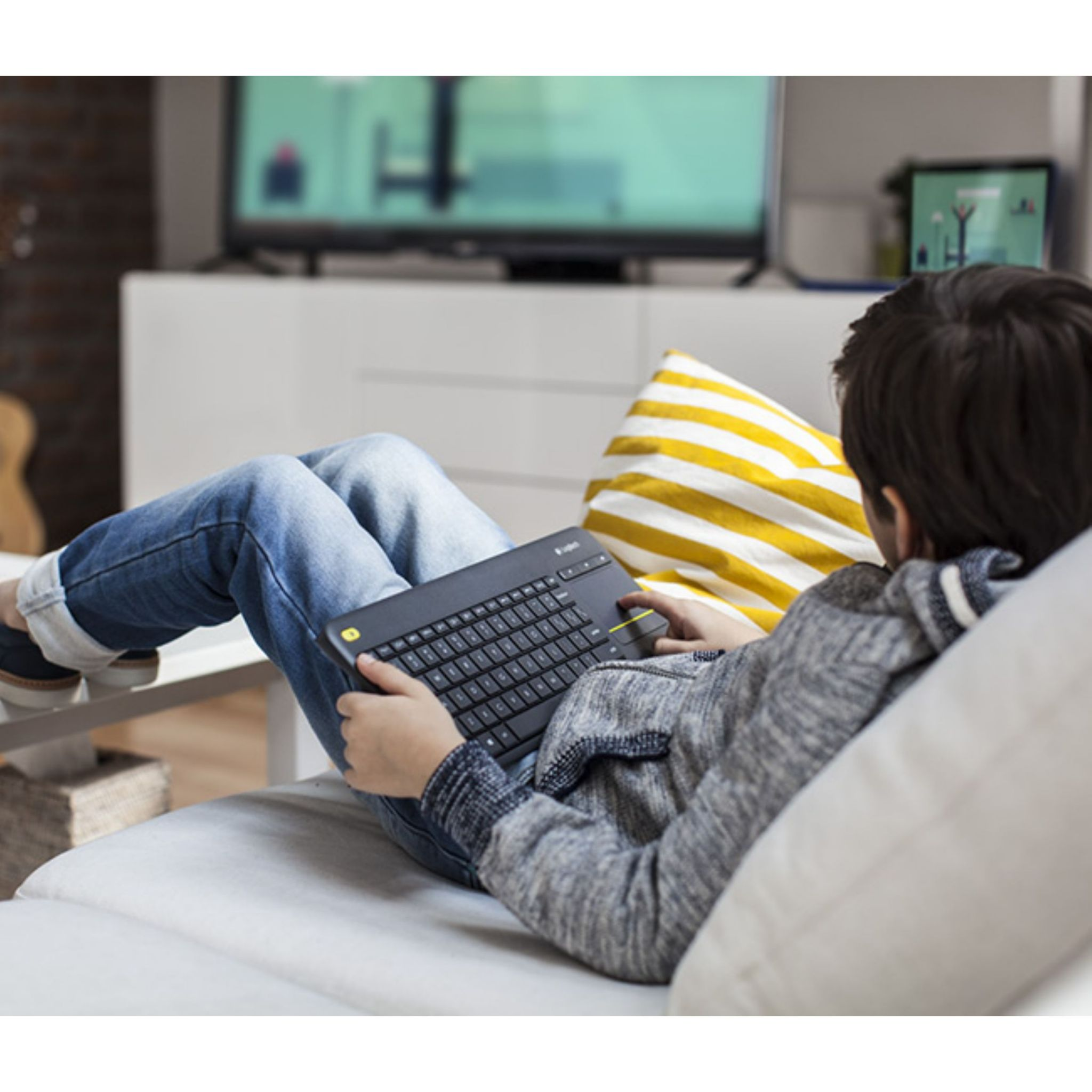 Een persoon gebruikt een zwart toetsenbord op een bank, met een tv op de achtergrond.